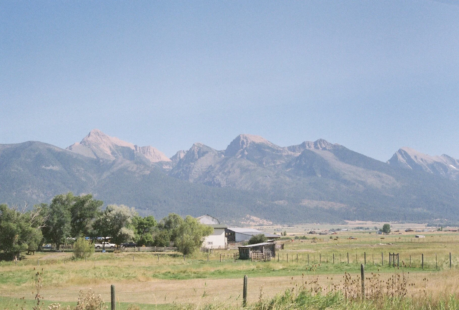 Mountains in the distance with a farm and green fields in the foreground.