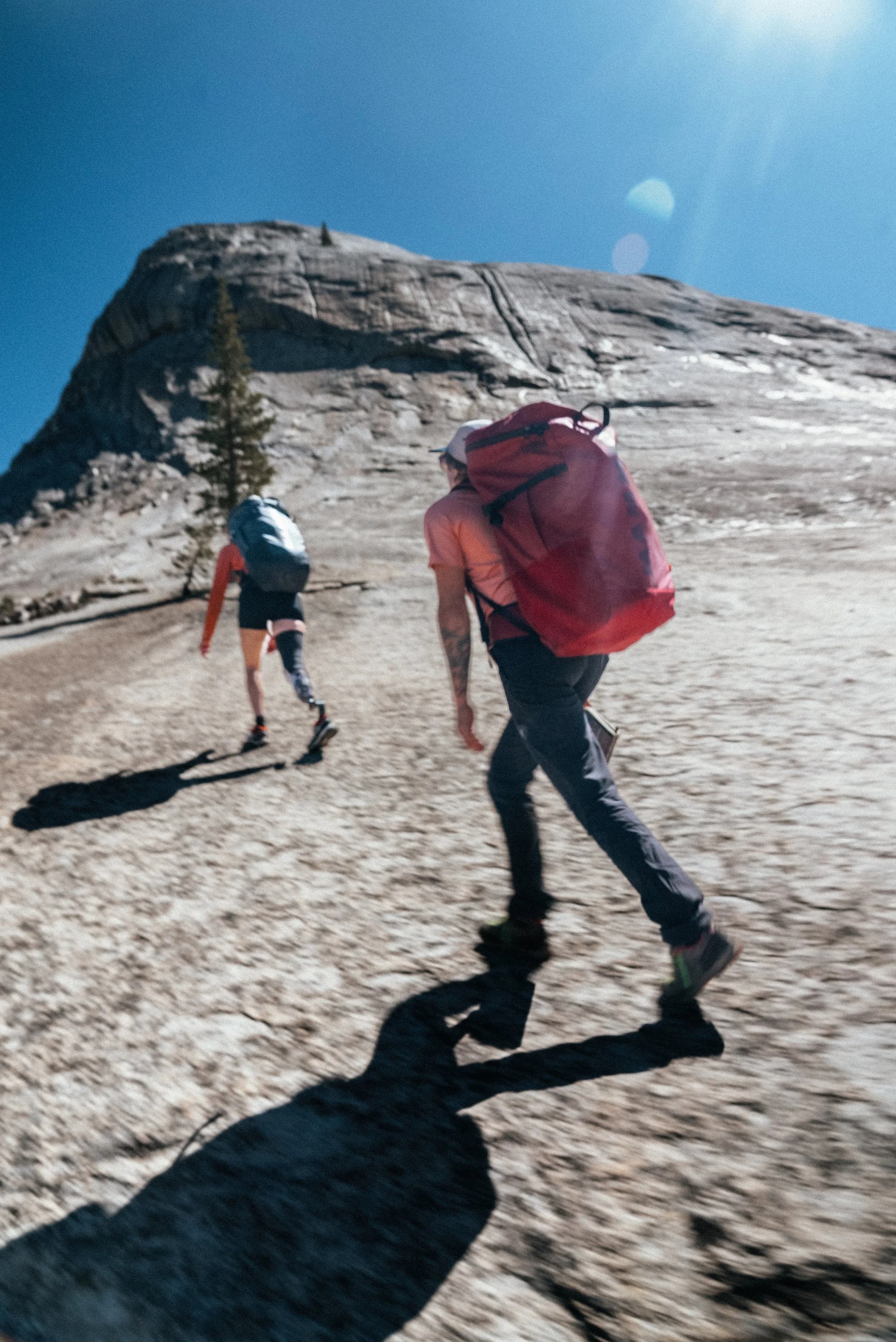 Two hikers climbing a rocky mountain slope under a bright blue sky.