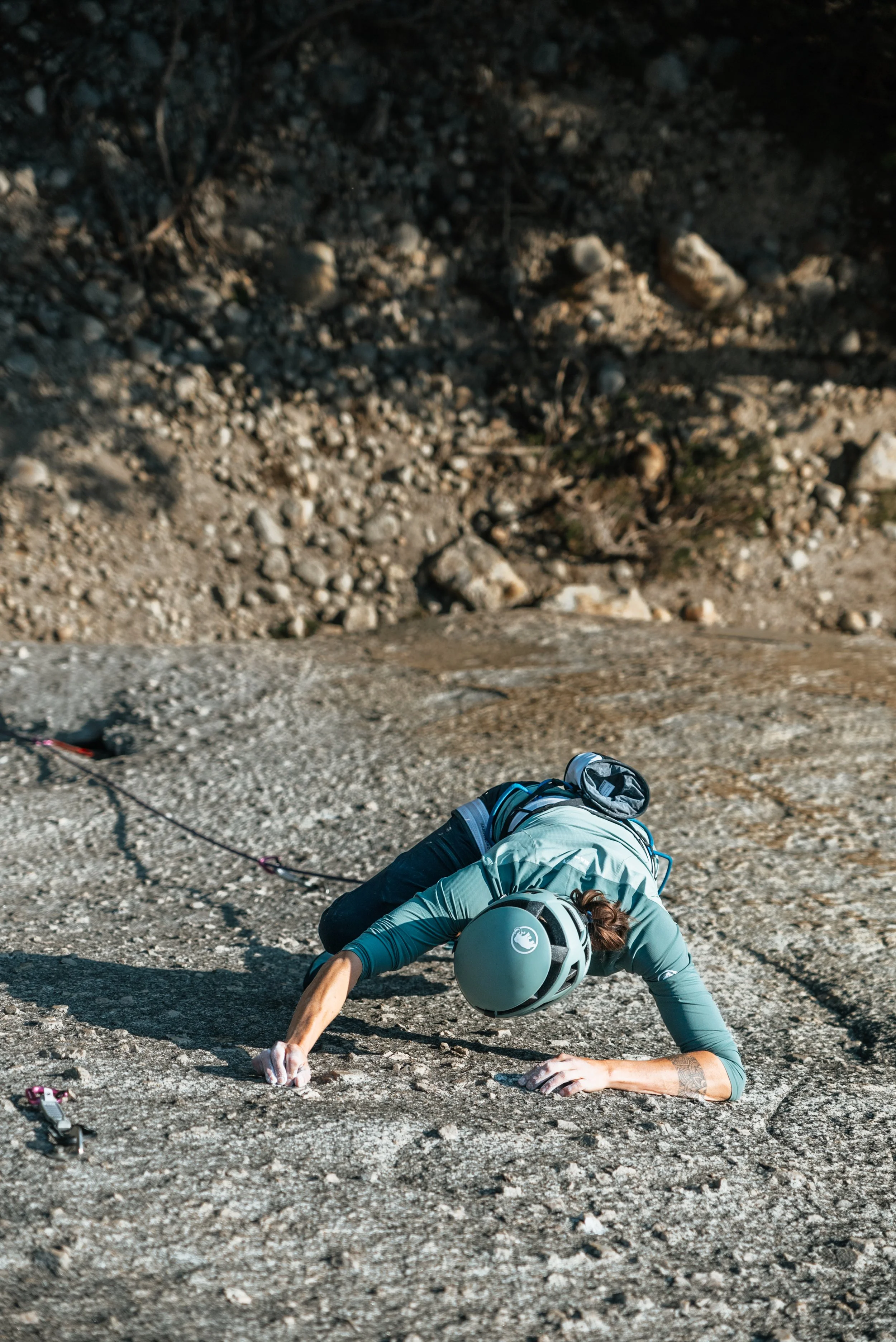 Person rock climbing outdoors on a steep, rocky surface, wearing a helmet and climbing gear.