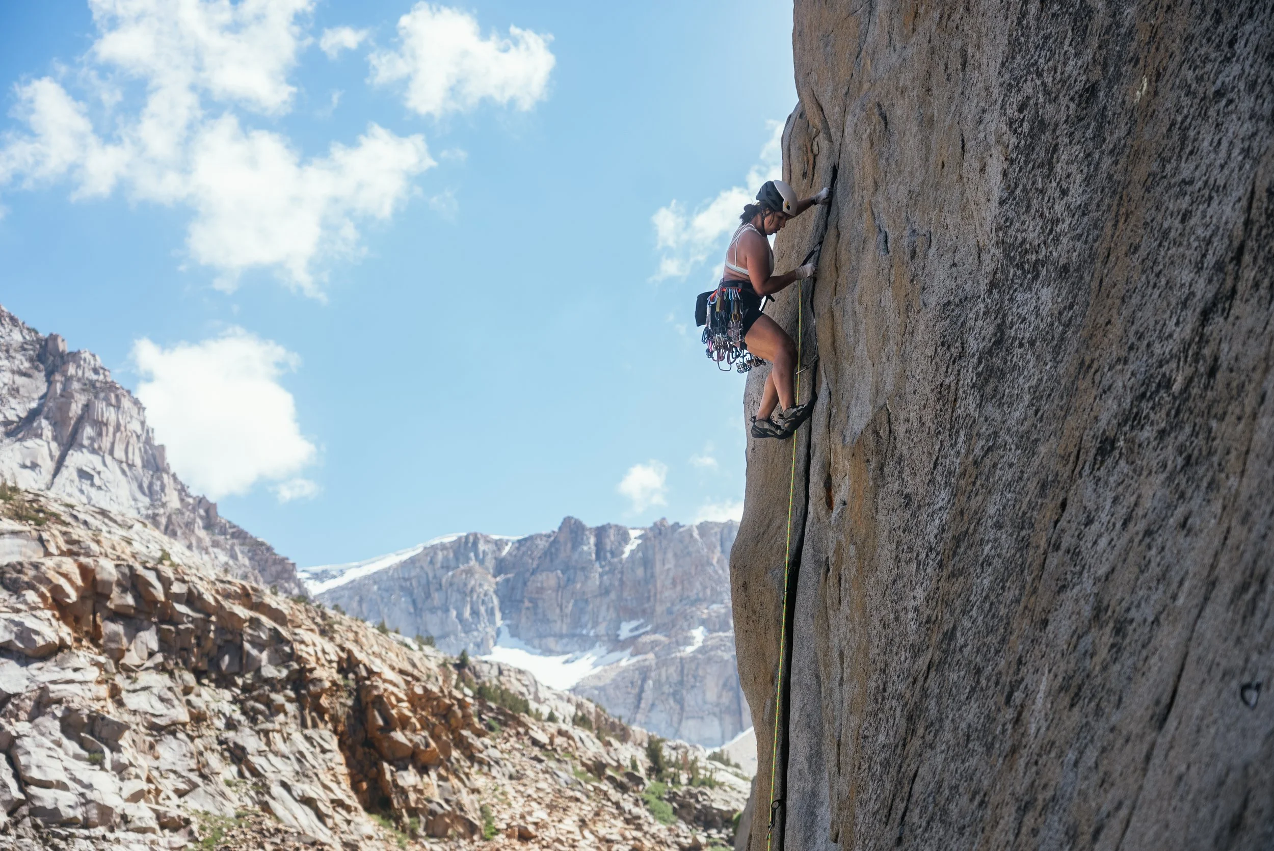 Person rock climbing on a steep cliffside in a mountainous area with snowy peaks in the background.