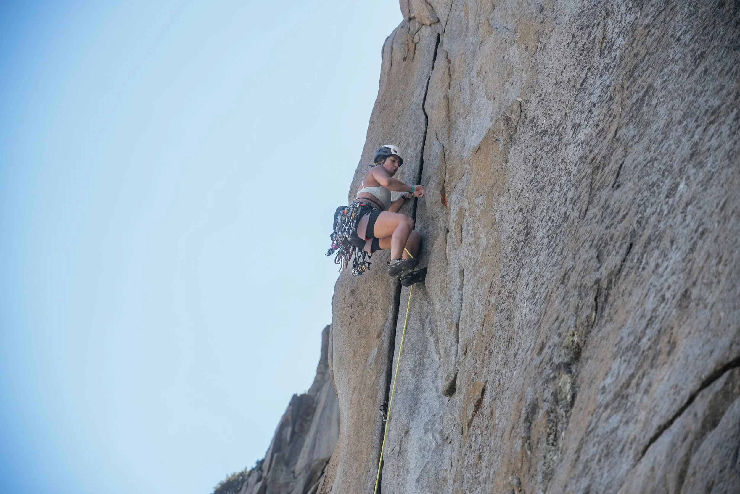 A woman rock climbing on a steep rock face wearing a helmet and climbing gear.