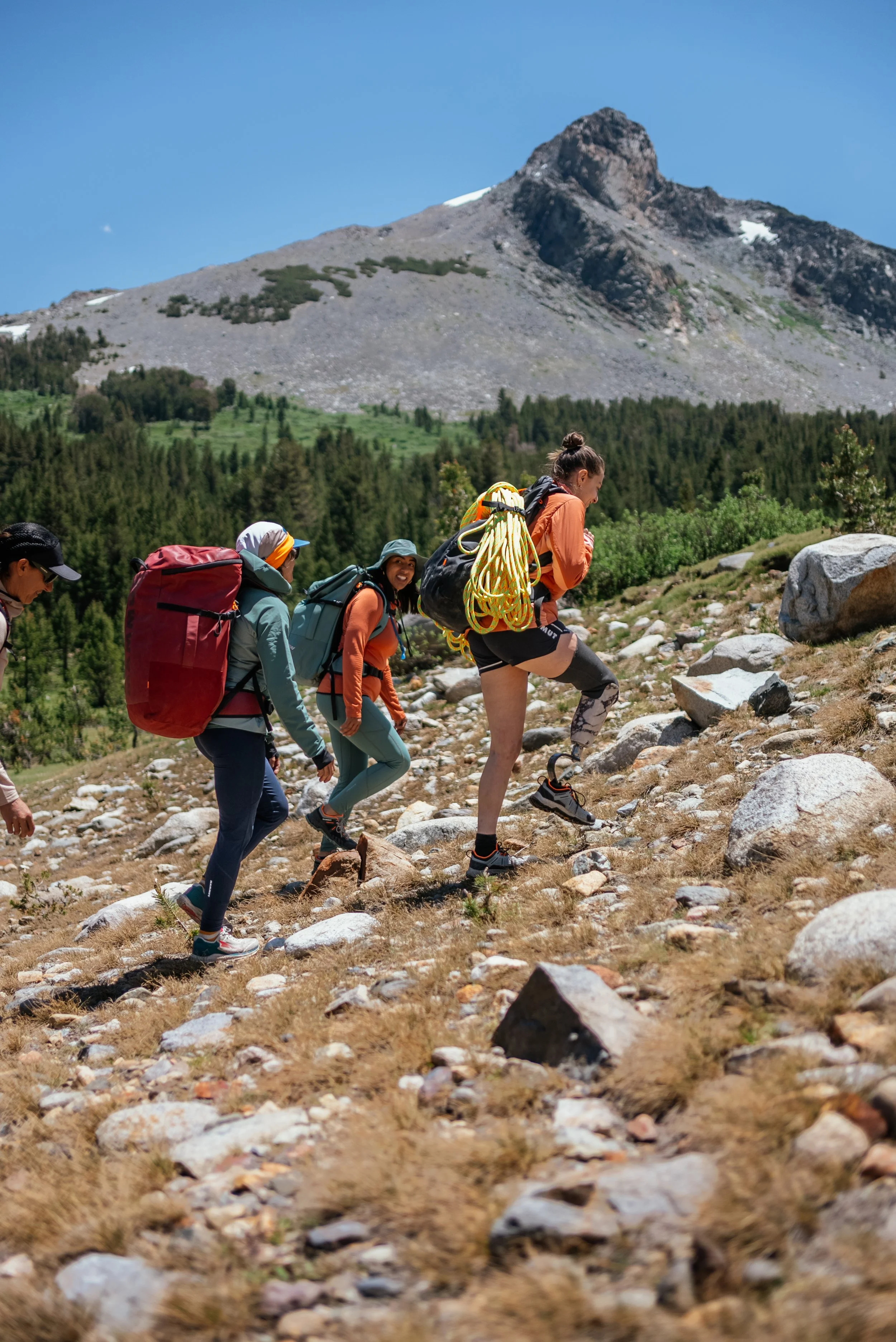 Group of four hikers trekking up a rocky mountain trail with a scenic mountain and forest in the background.