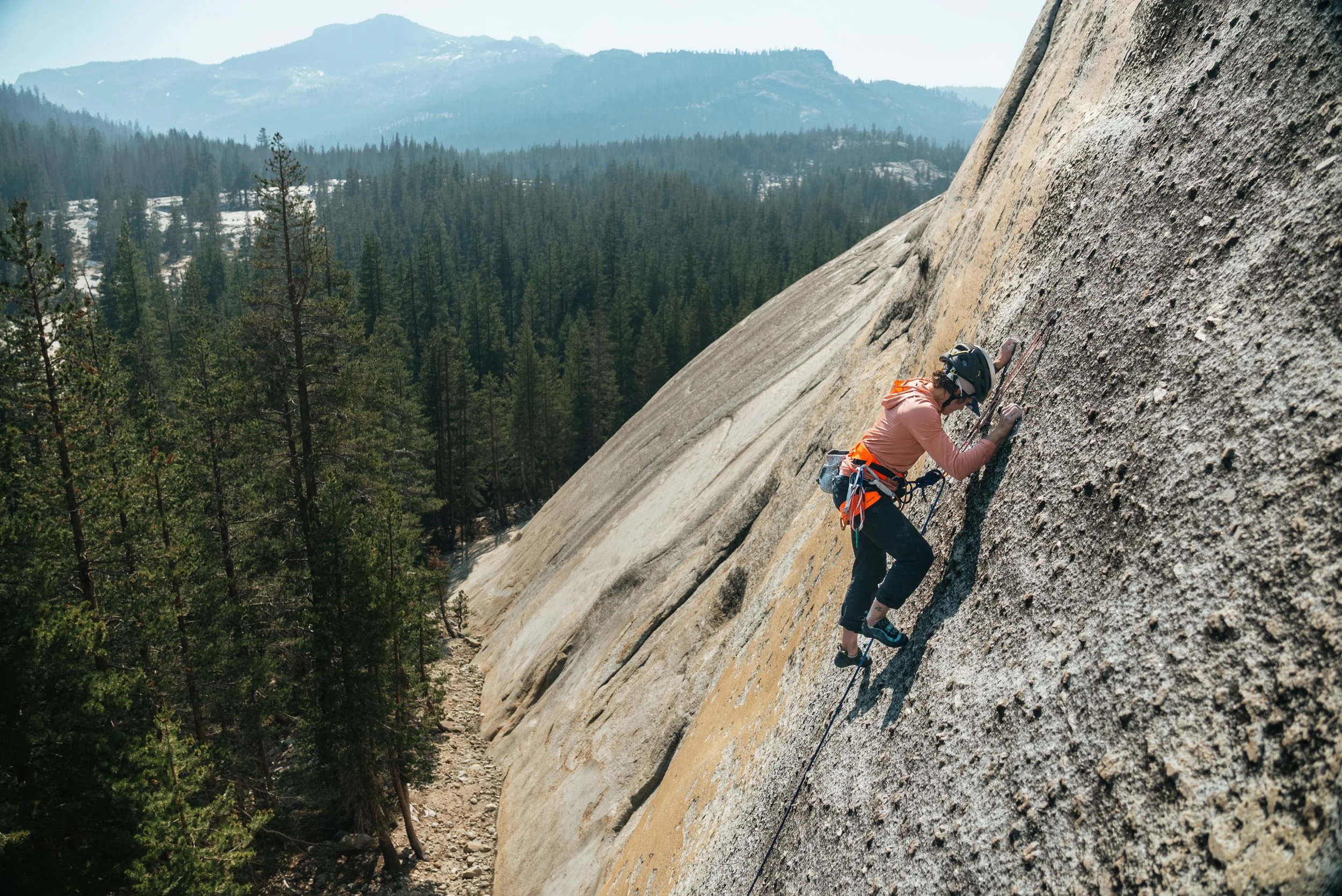 Person rock climbing on a steep granite wall in a mountainous forest area
