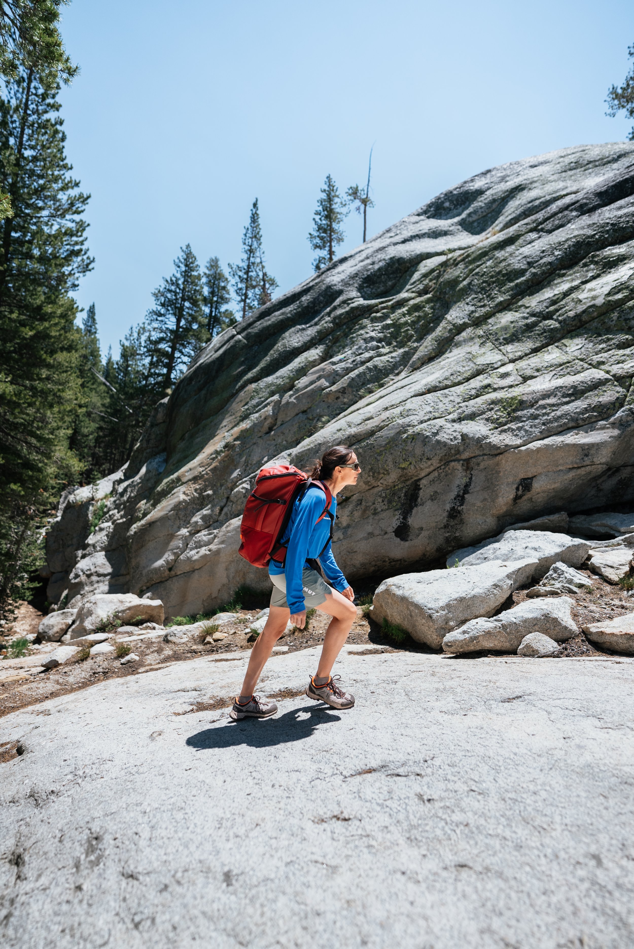 A woman hiking on a rocky trail in a forested mountain area during daytime.