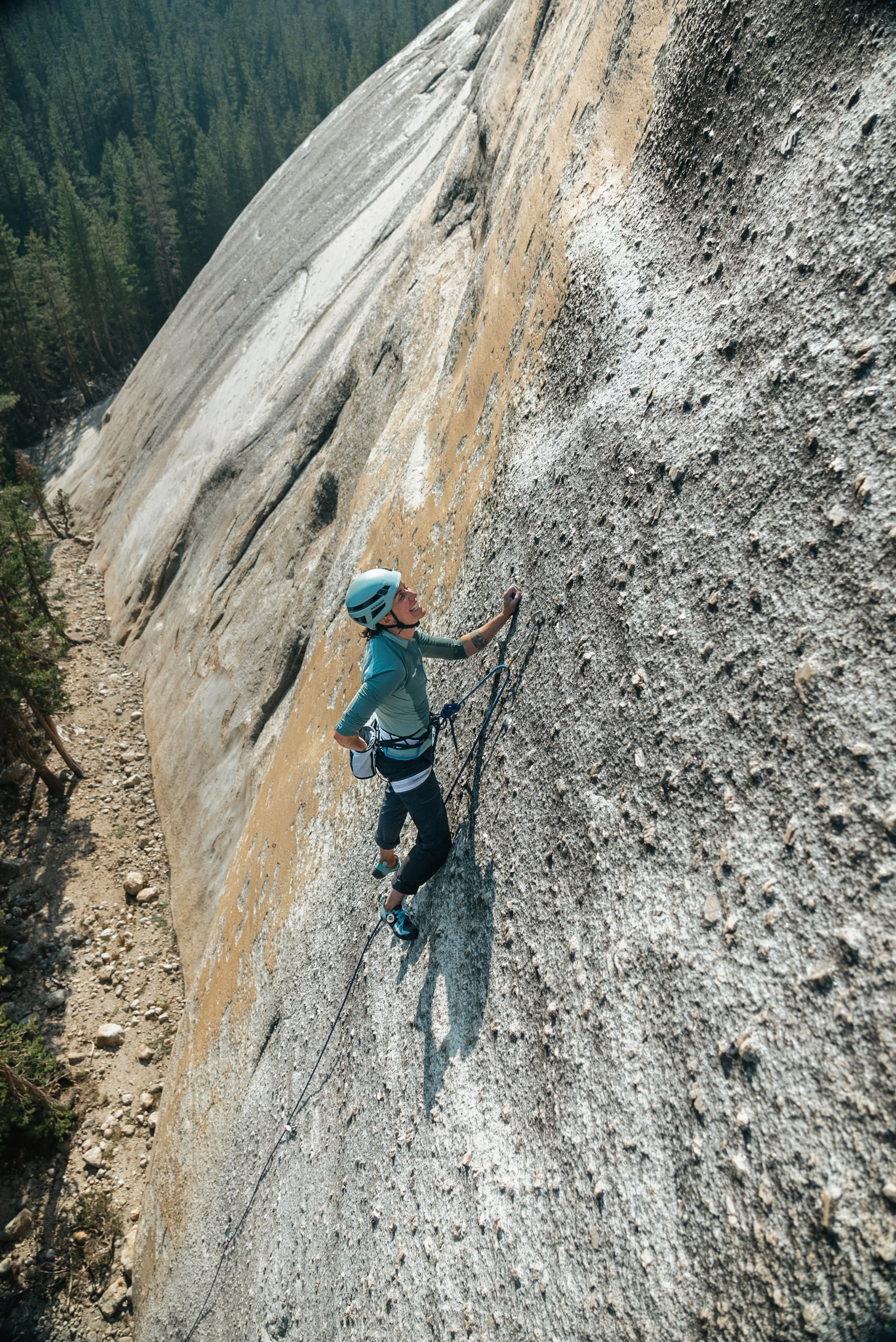 A person wearing a safety helmet and harness rock climbing on a steep granite wall outdoors.