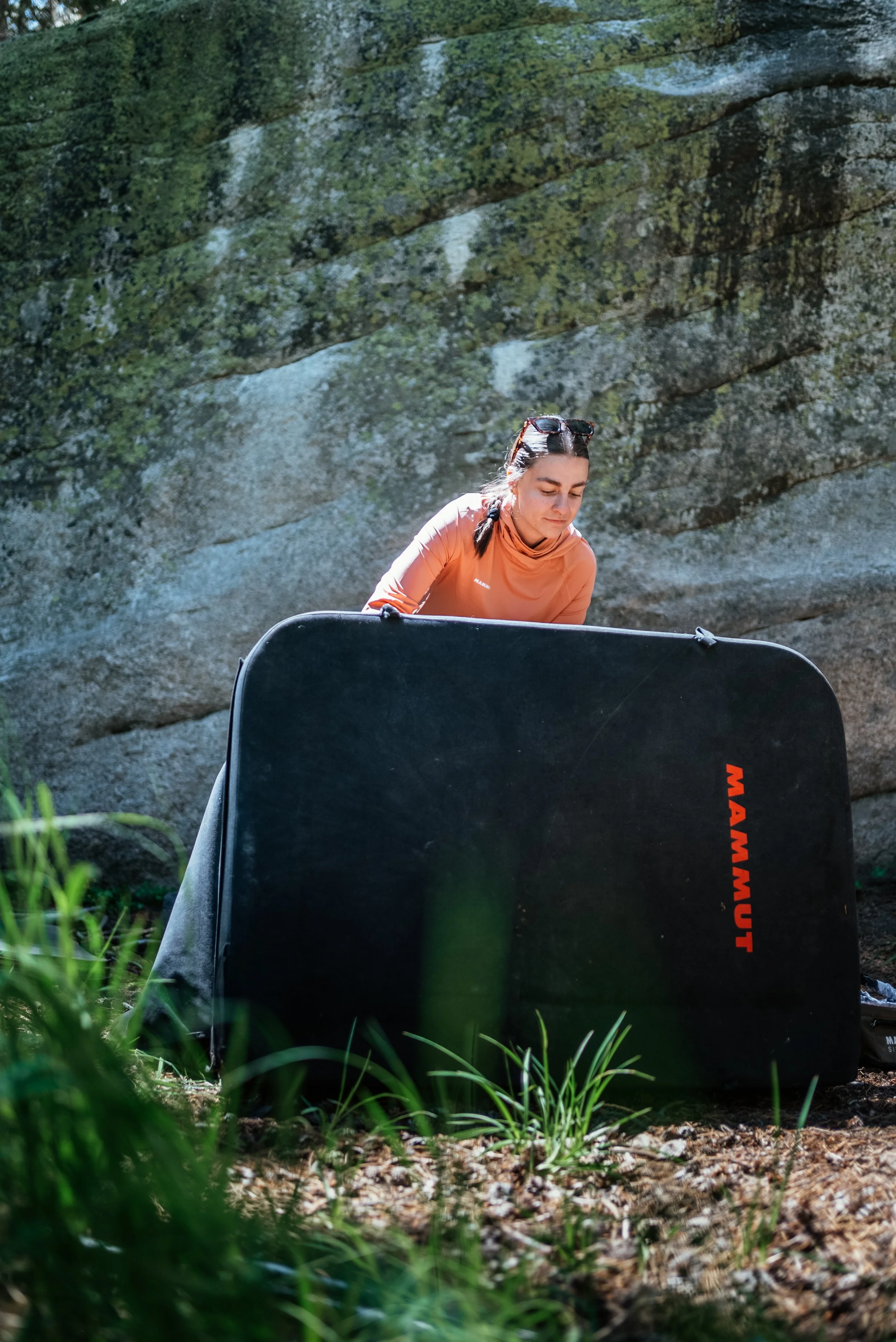 Woman setting up a large black camping or outdoor gear bag in a natural outdoor setting with rocks and greenery.
