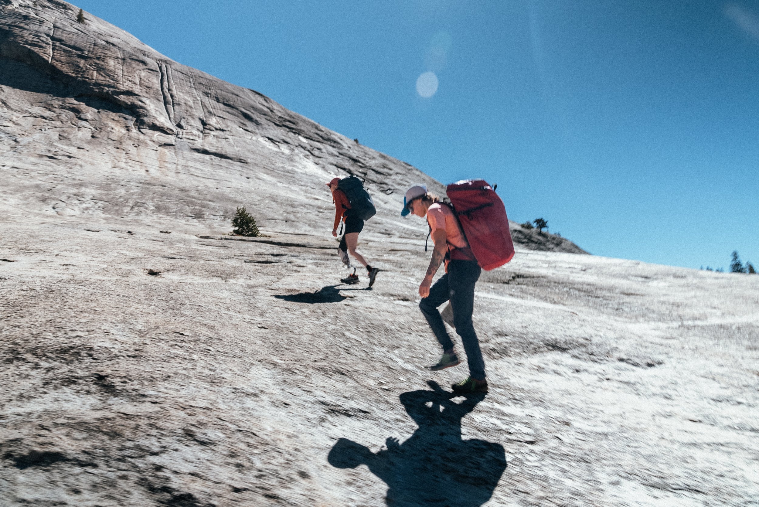 Two hikers climbing a steep, rocky mountain slope under a clear blue sky.