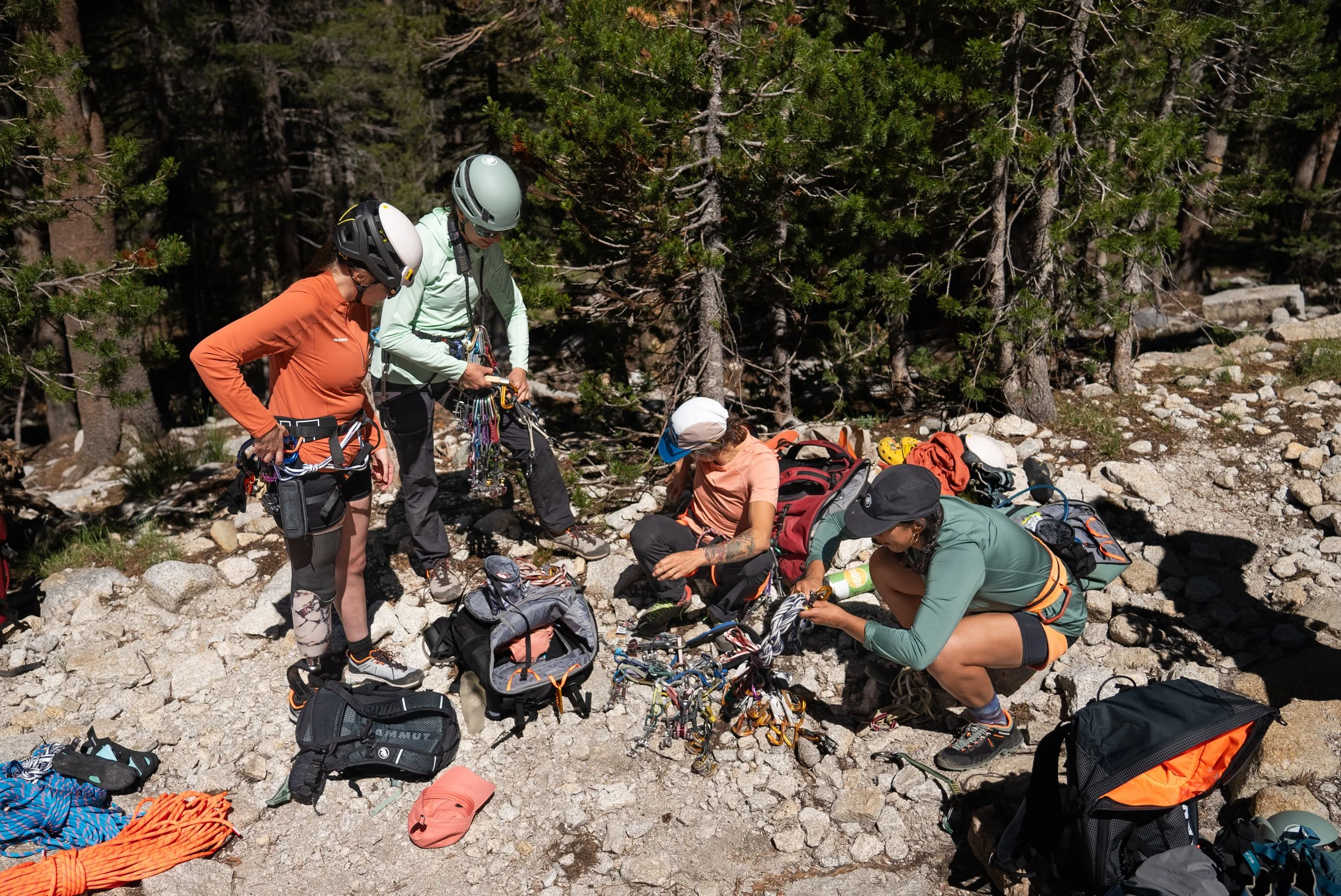 Group of five climbers preparing their gear on rocky ground with trees in the background.