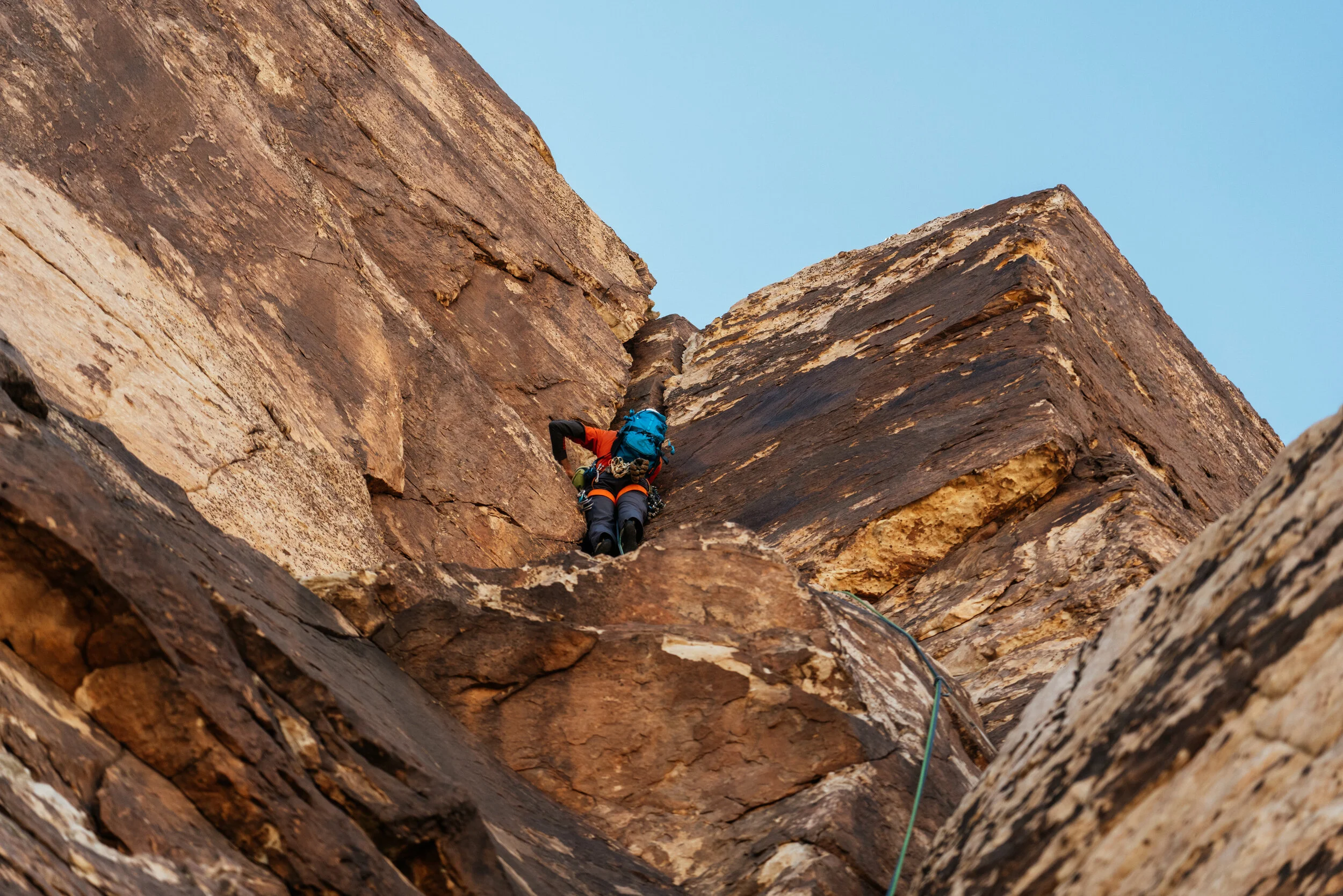 A person rock climbing on a steep, rugged cliff with a blue sky in the background.