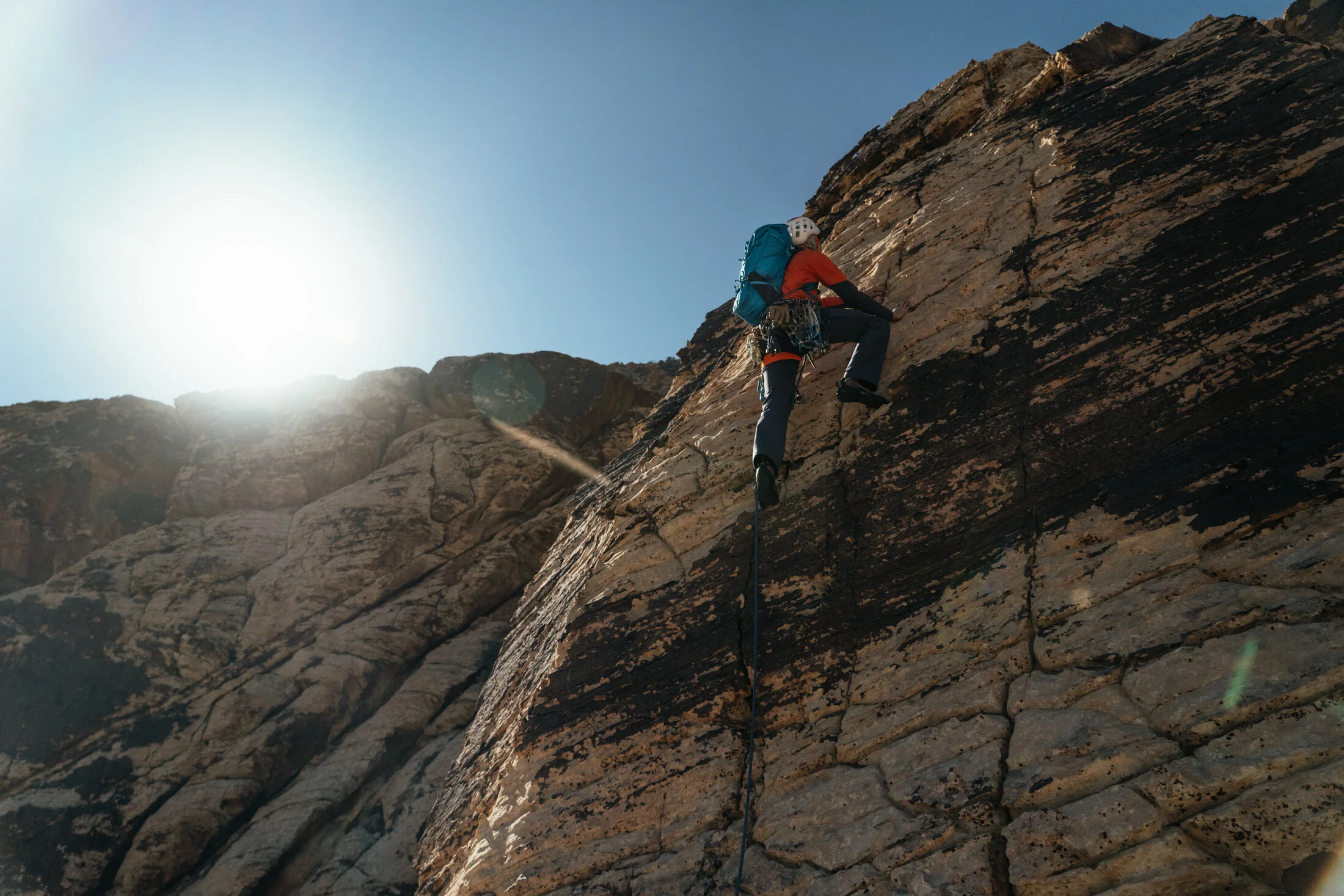 A person wearing a helmet and carrying a backpack is rock climbing on a steep cliff.