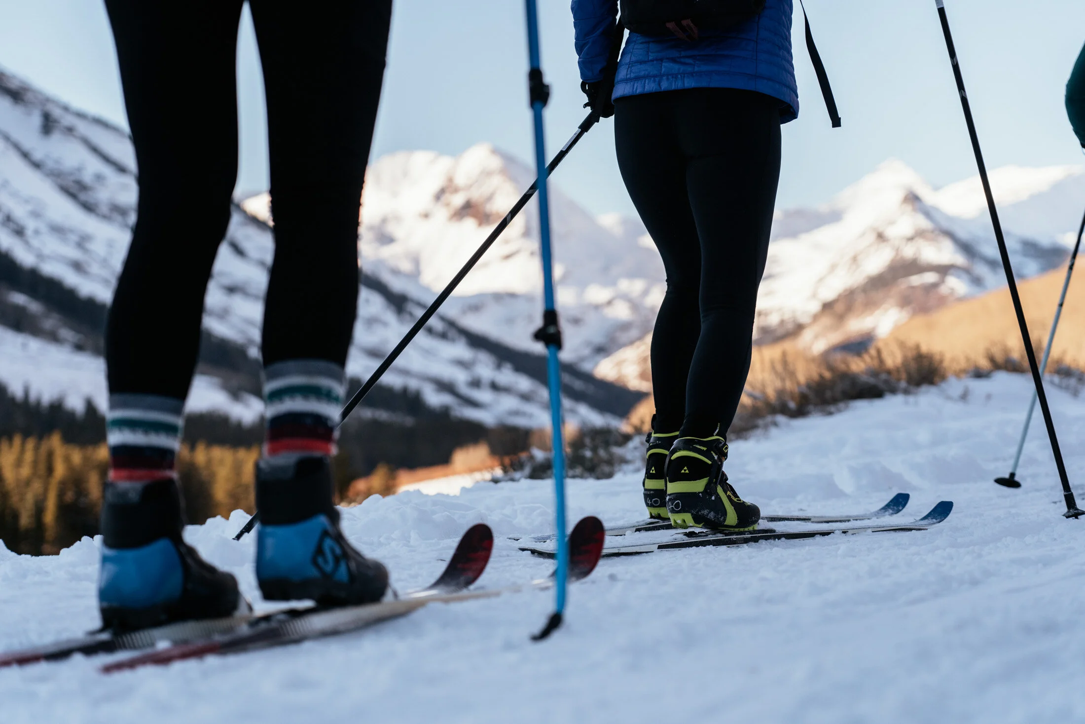 Close-up of two people skiing on snow with mountains in the background.