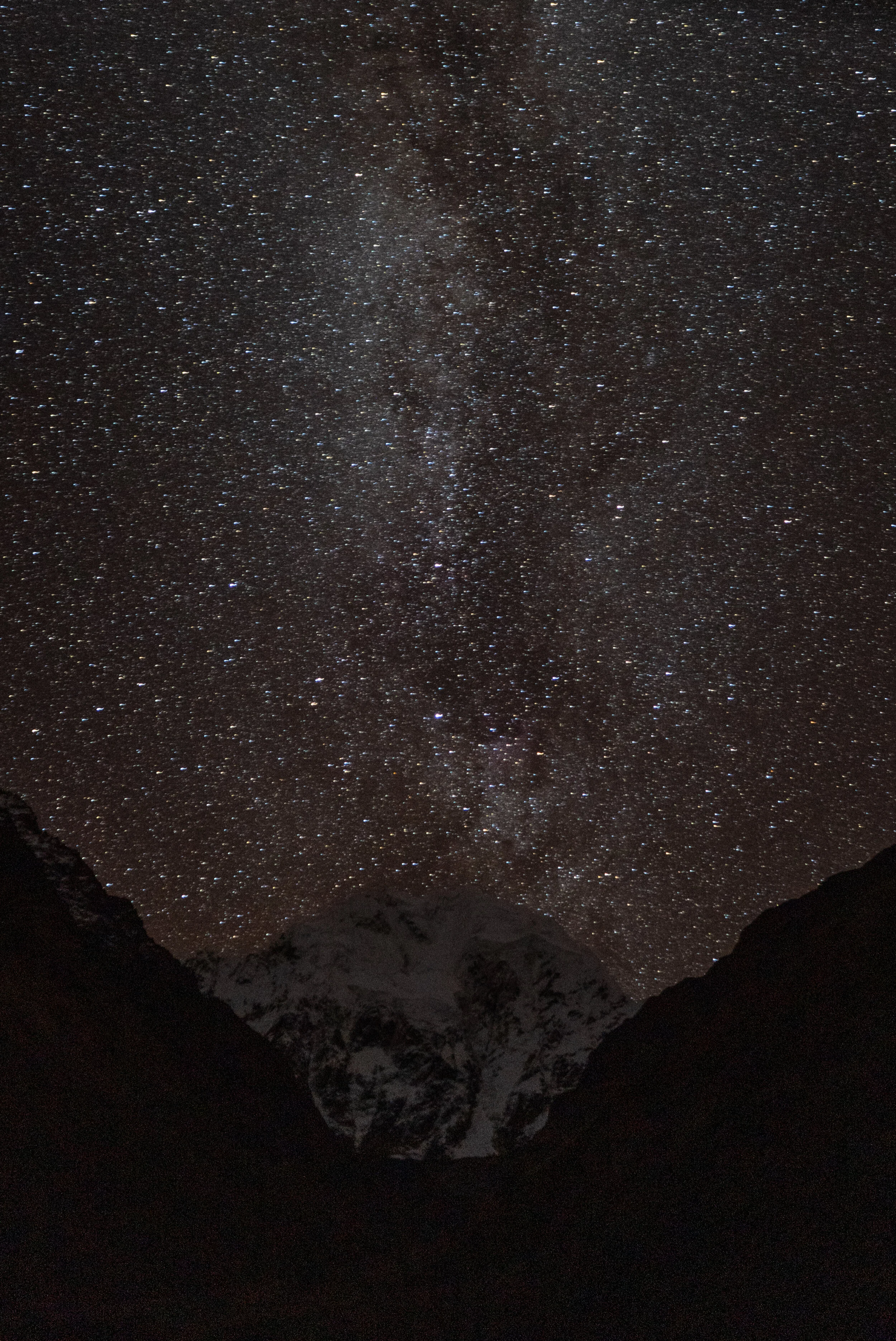 Nighttime view of a starry sky above snow-capped mountains, with the Milky Way galaxy visible.