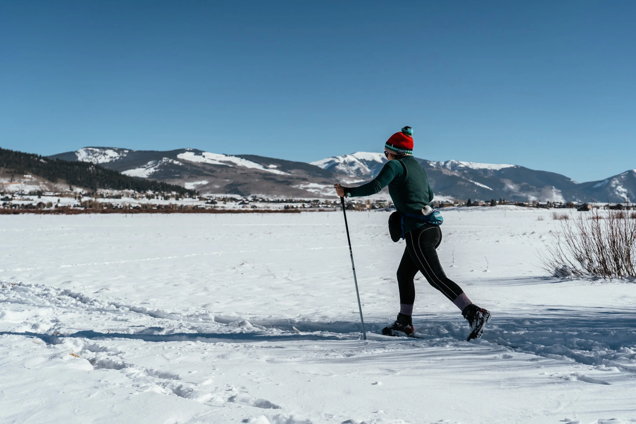 Person cross-country skiing on snow-covered landscape with mountains in the background.