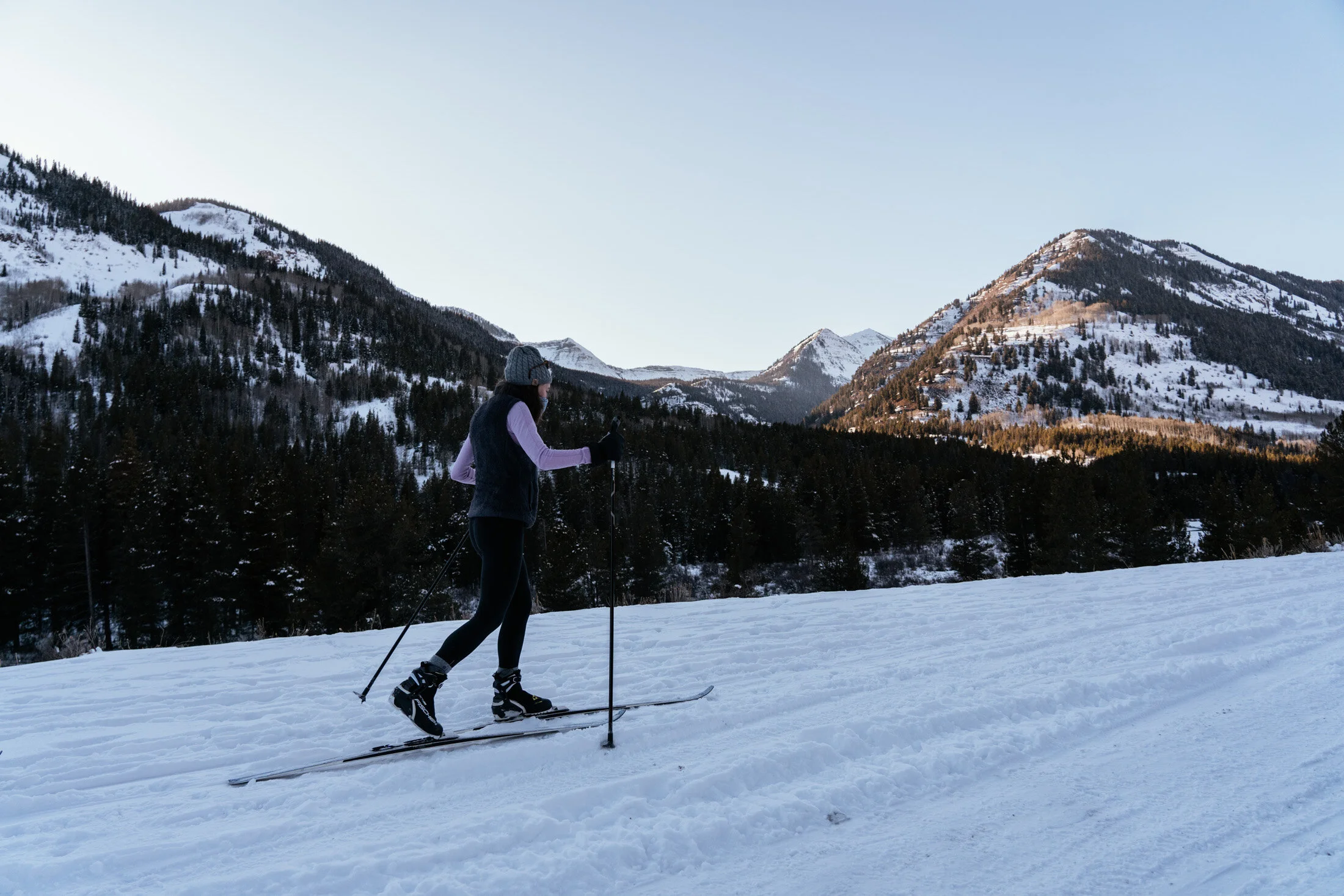 A woman cross-country skiing on snow-covered terrain with a mountain range in the background.
