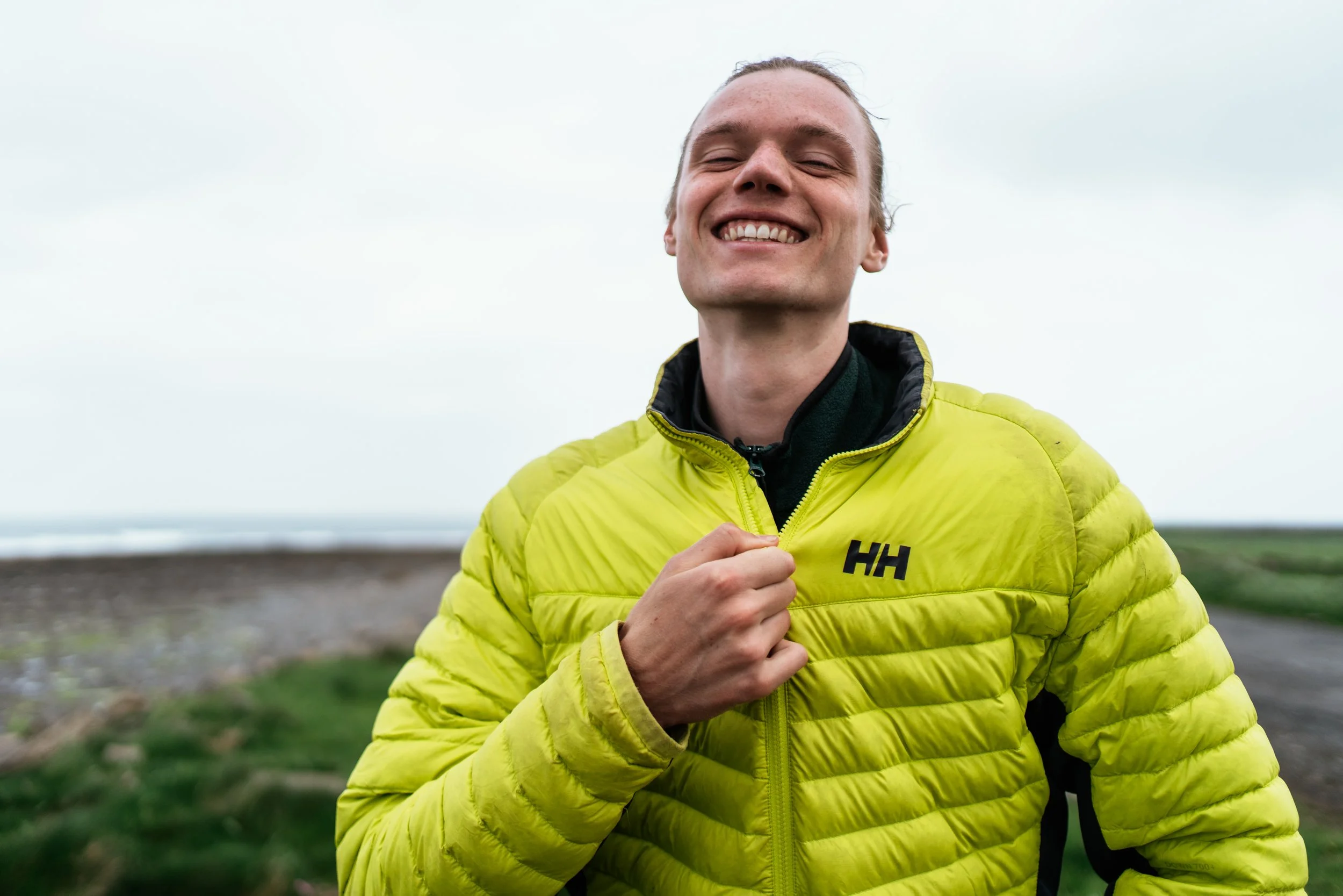 Smiling man wearing a bright yellow puffy jacket outdoors on a cloudy day.