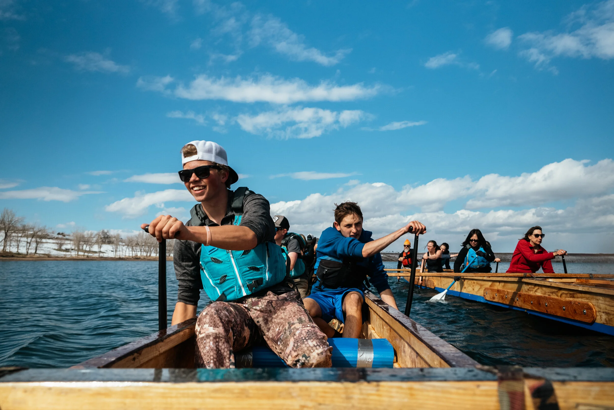 People rowing in a wooden boat on a lake under a blue sky with clouds.