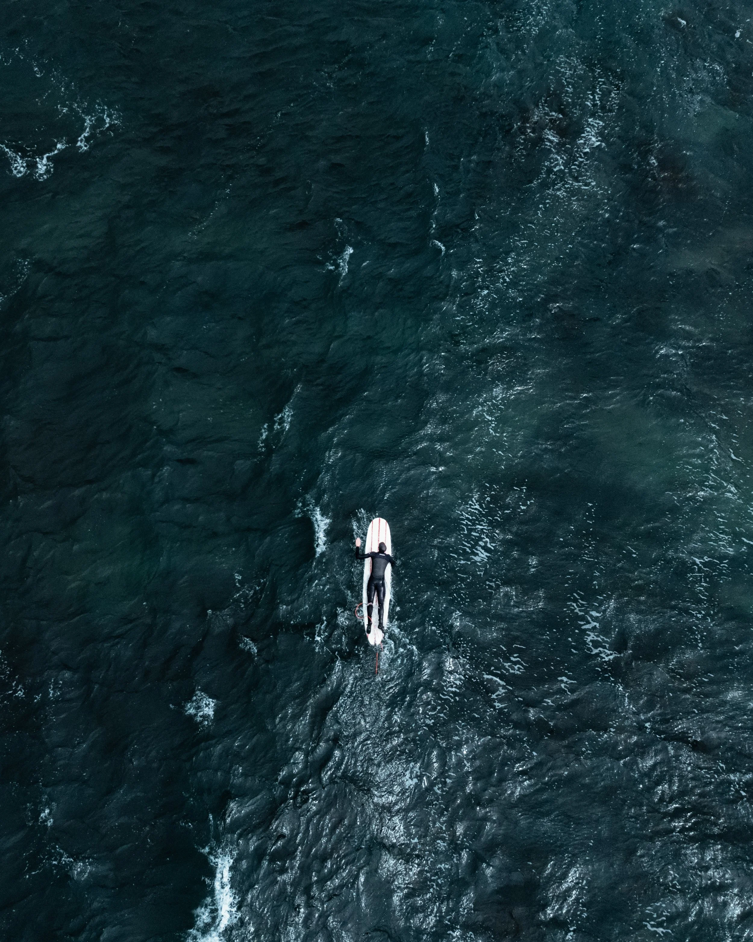 A person surfing on a wave in the ocean, seen from above.