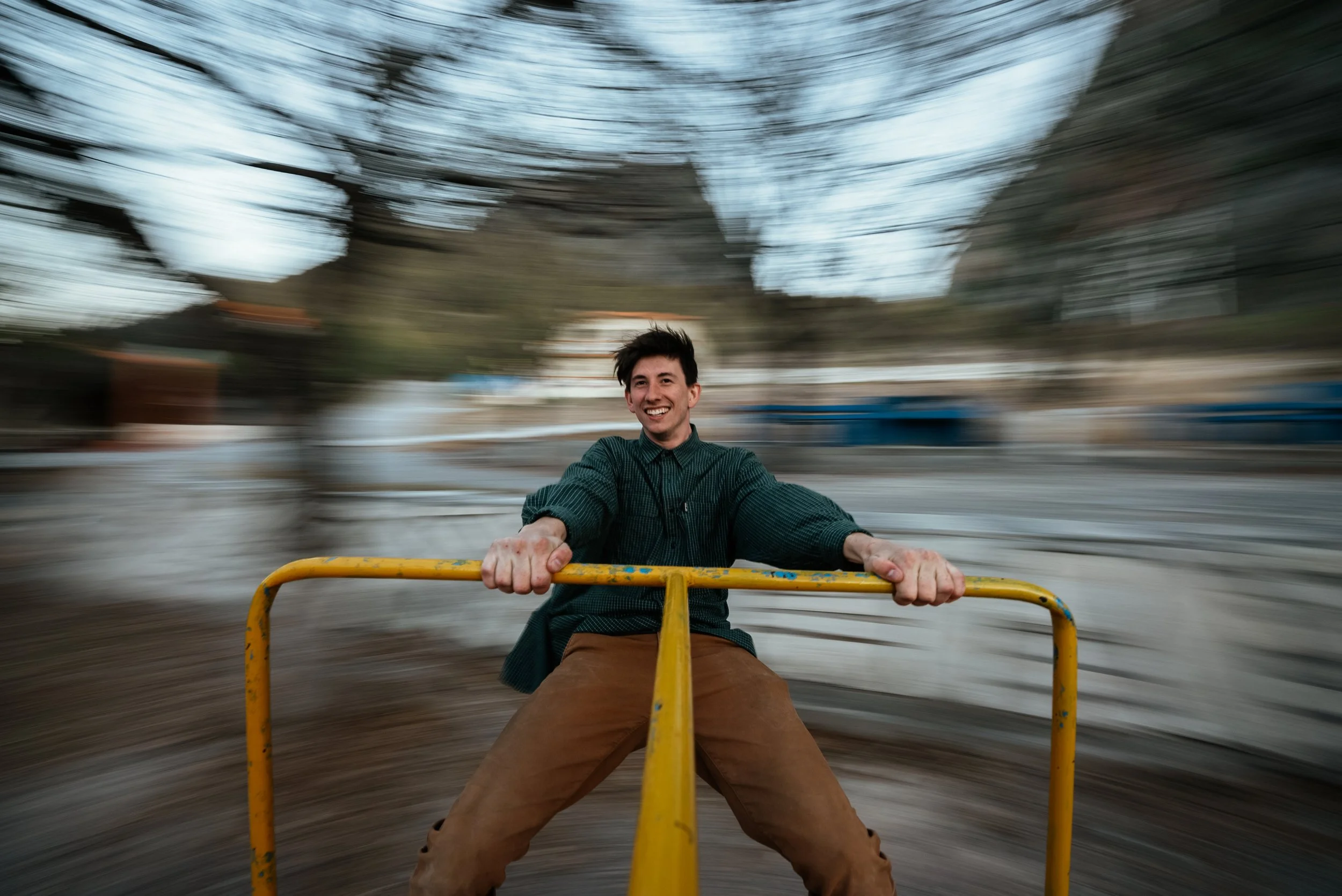 A young man smiling and holding onto a yellow railing on a spinning amusement park ride, with motion blur in the background indicating rotation.
