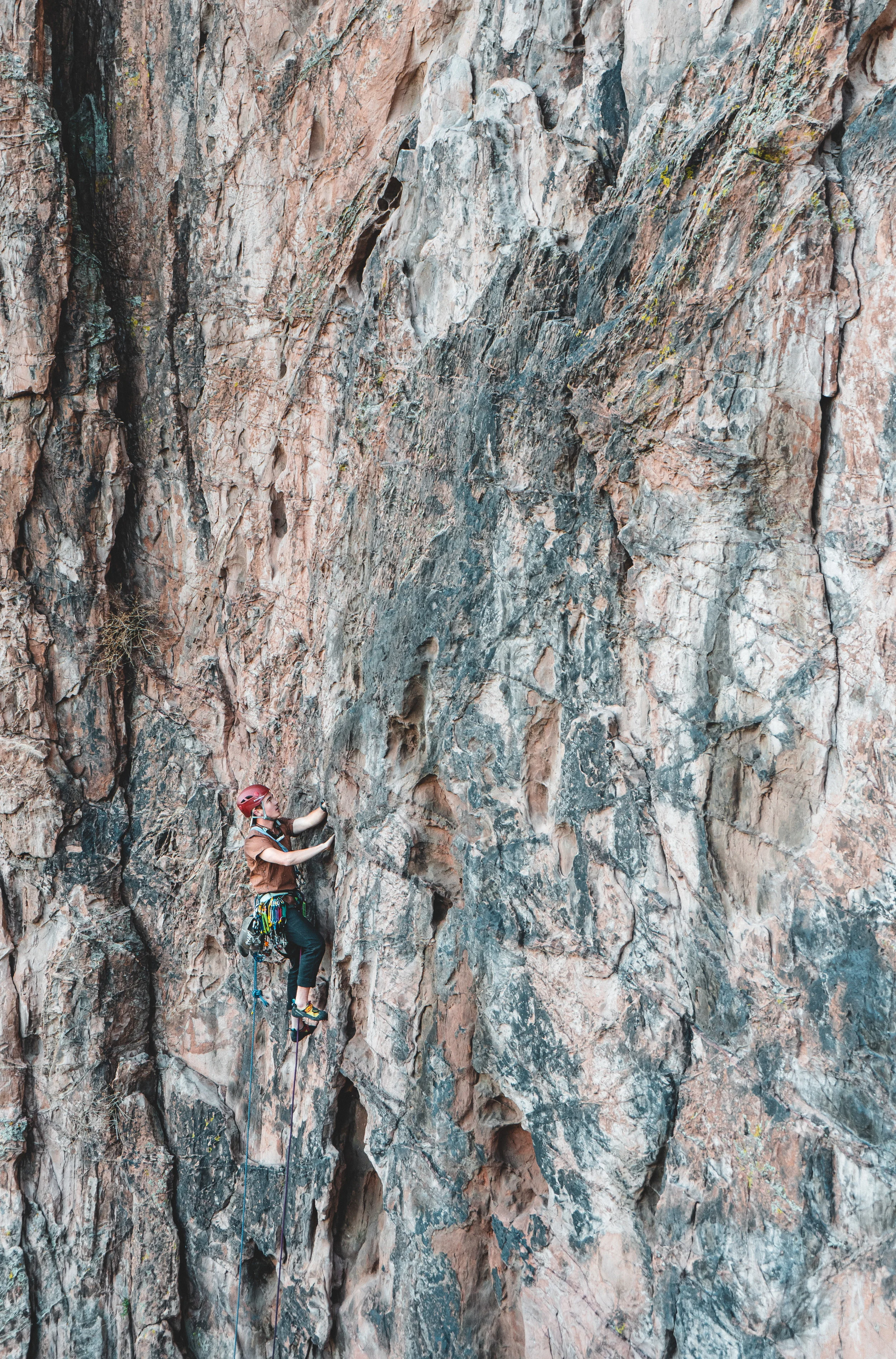 A person wearing a helmet and climbing gear scaling a large, rugged rock face outdoors.