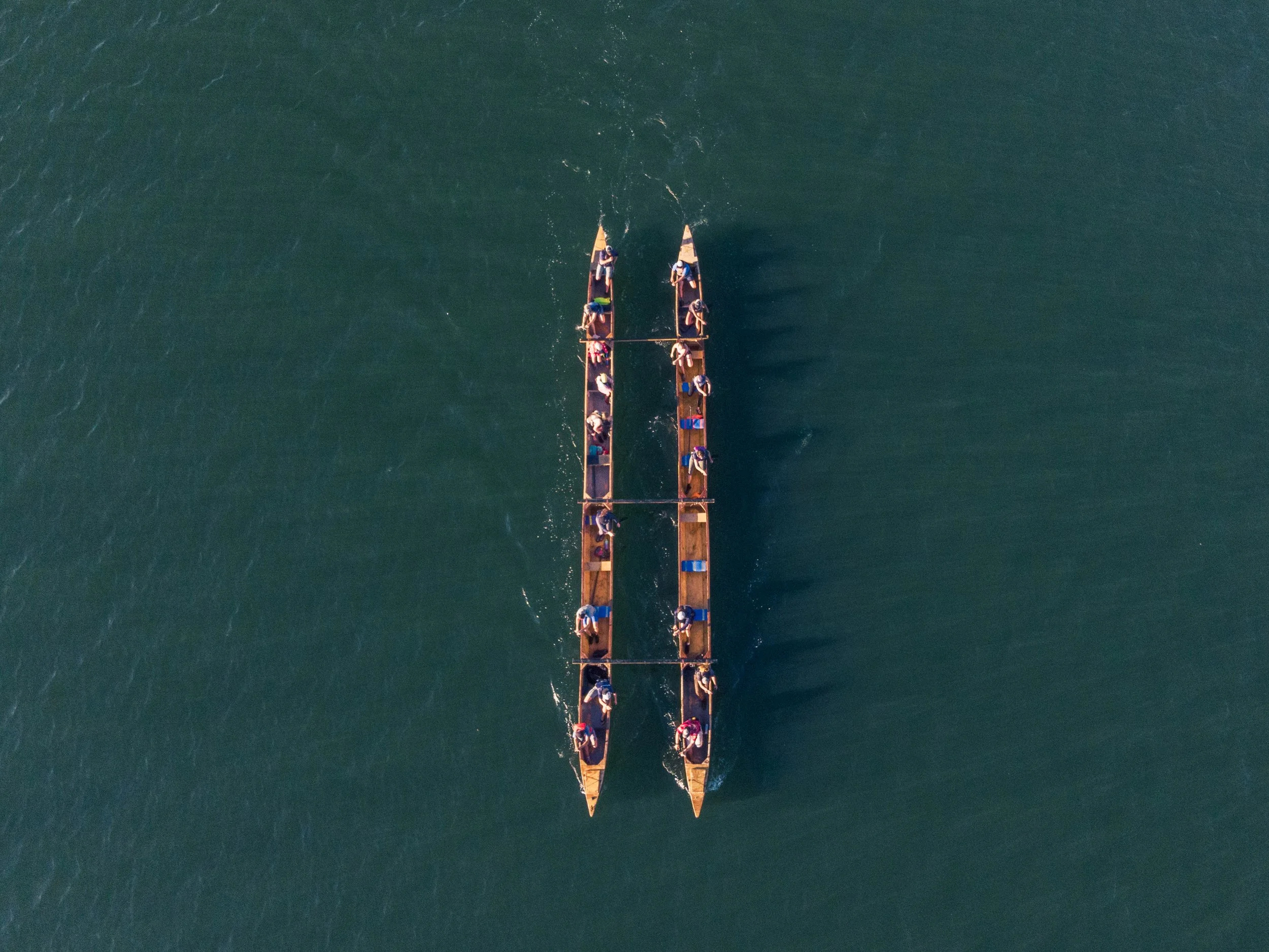 An aerial view of two long wooden boats with rowers practicing on calm water.