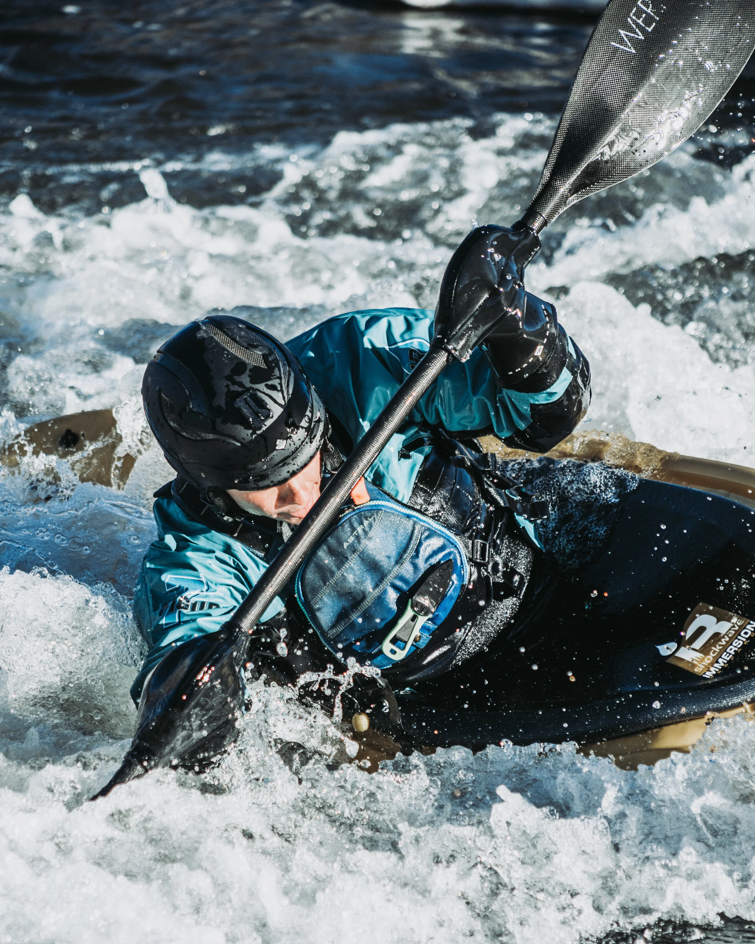 Person wearing a helmet and life jacket kayaking through white water rapids.