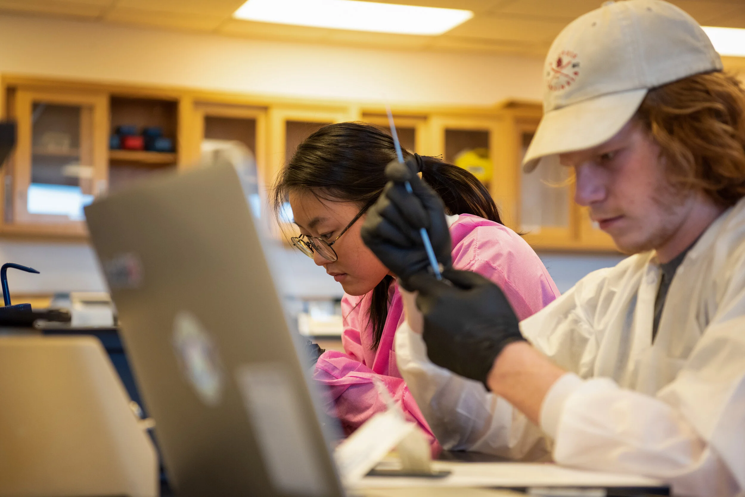 Two students working together in a science lab, with one holding a pipette.
