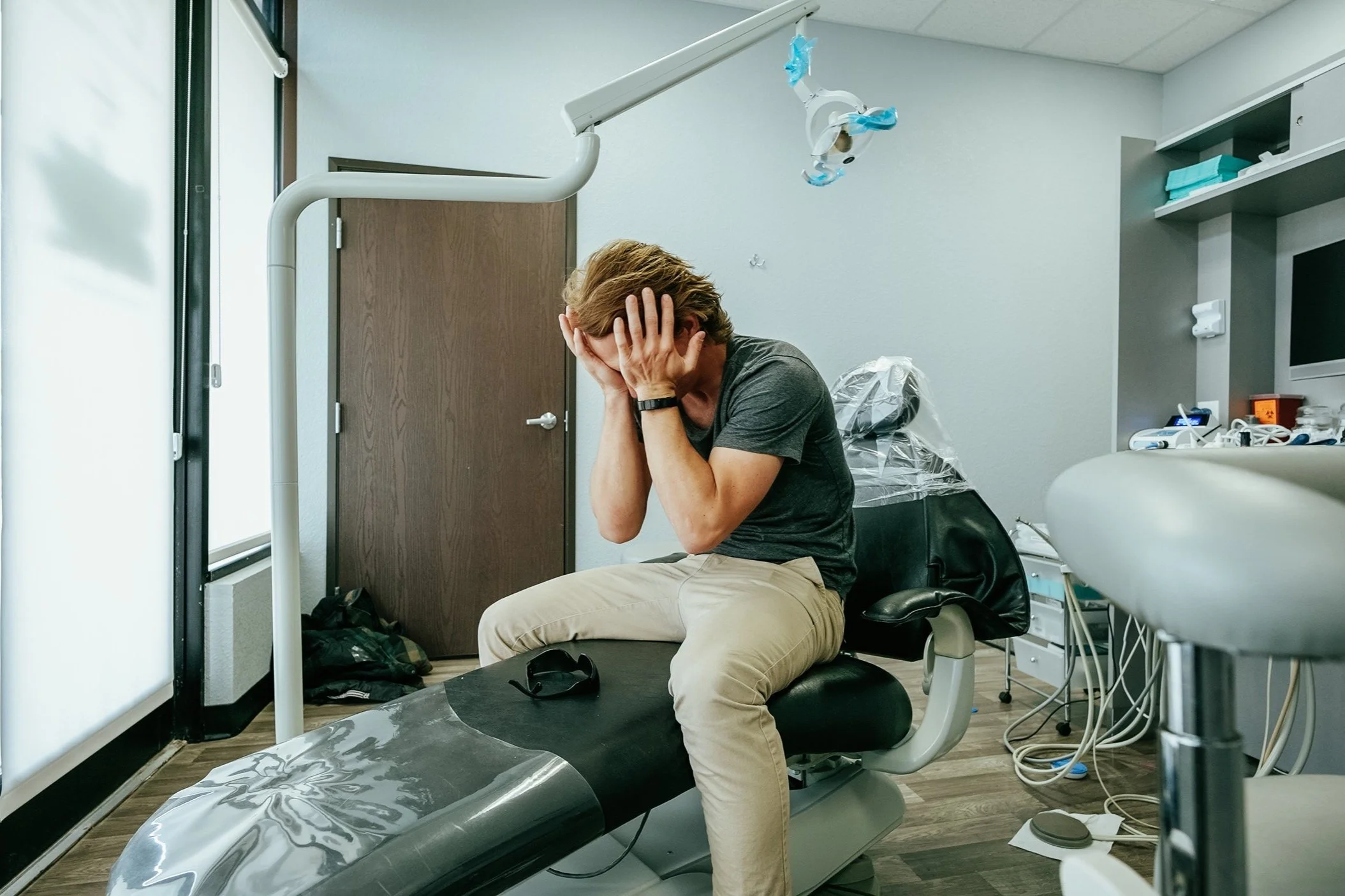 Person sitting on medical examination table with hand on their head in a doctor's office