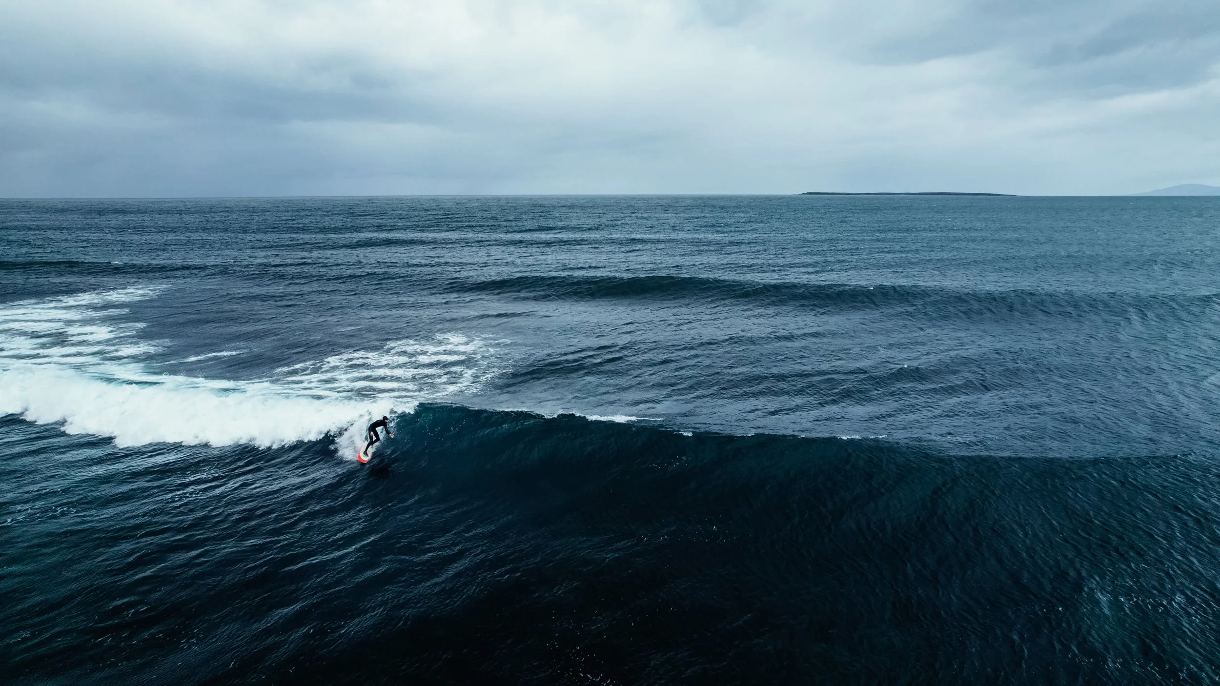 A person surfing on a wave in the ocean on a cloudy day.