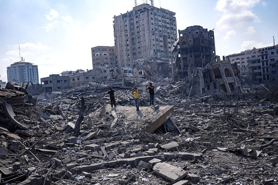 People standing amidst the rubble of a destroyed city, with damaged buildings in the background.