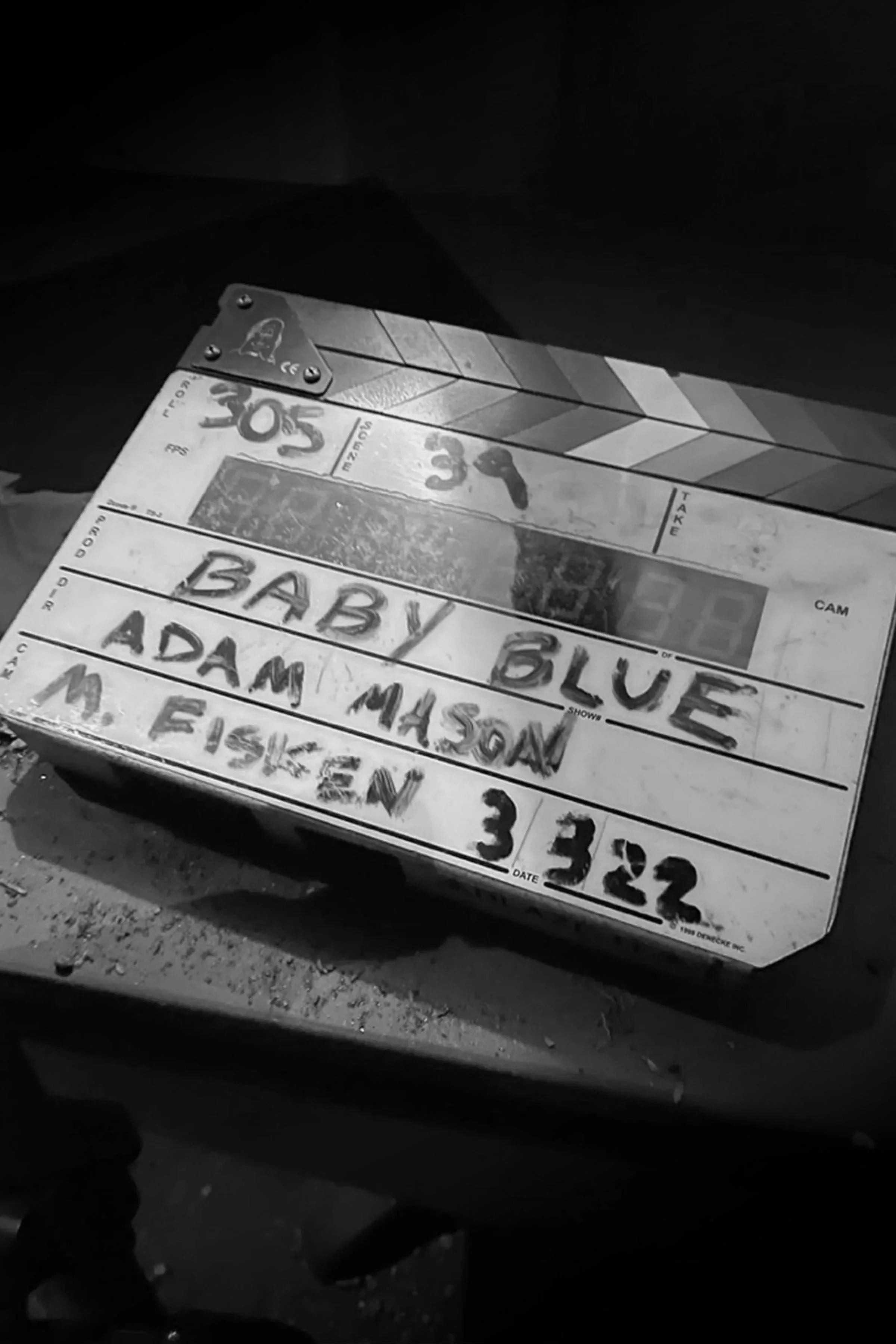 Clapperboard and handwritten notes on a paper with the text 'Baby Blue' and 'Adam Mason' visible, placed on a rough surface.