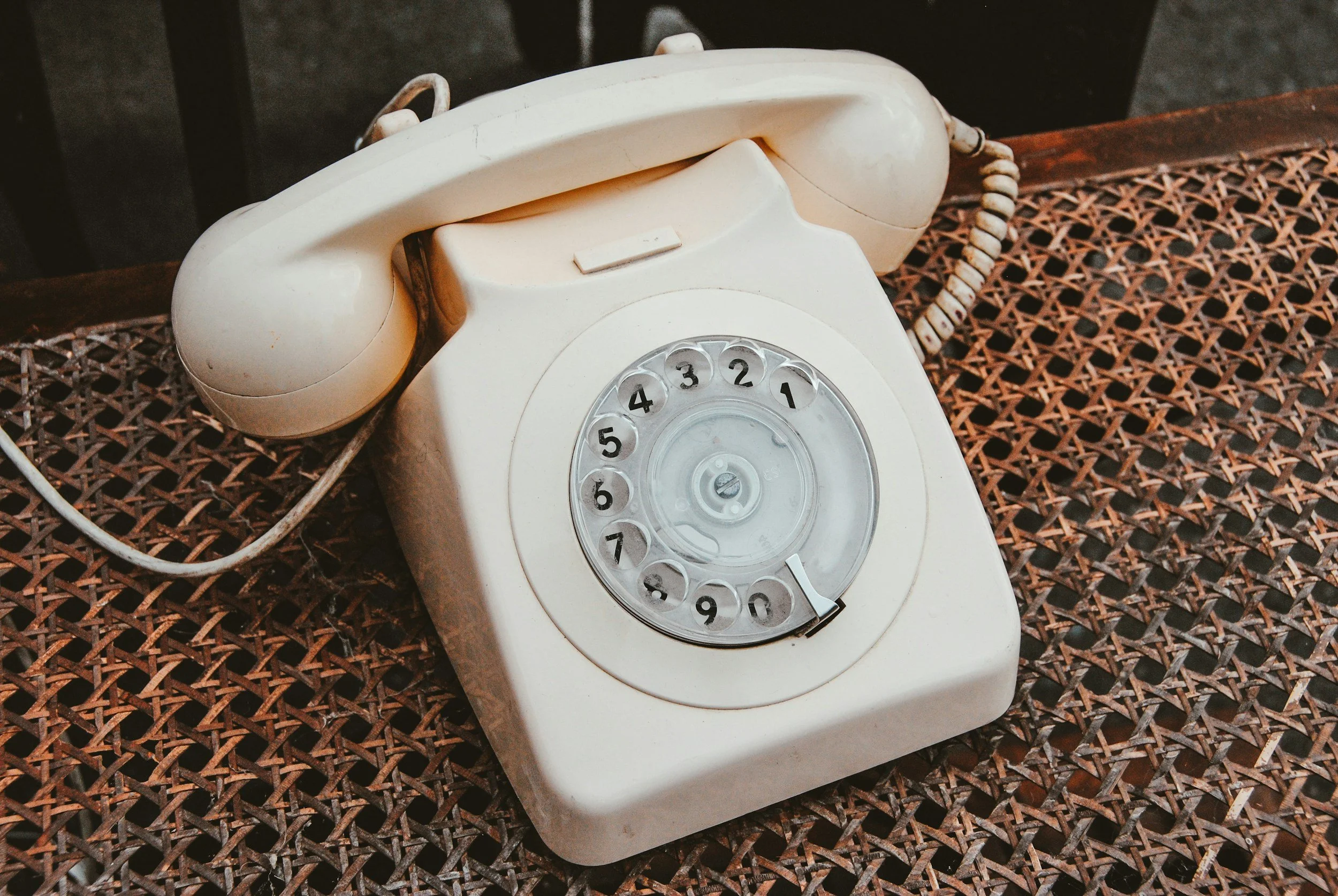 An old-fashioned rotary dial telephone in beige color placed on a woven surface.