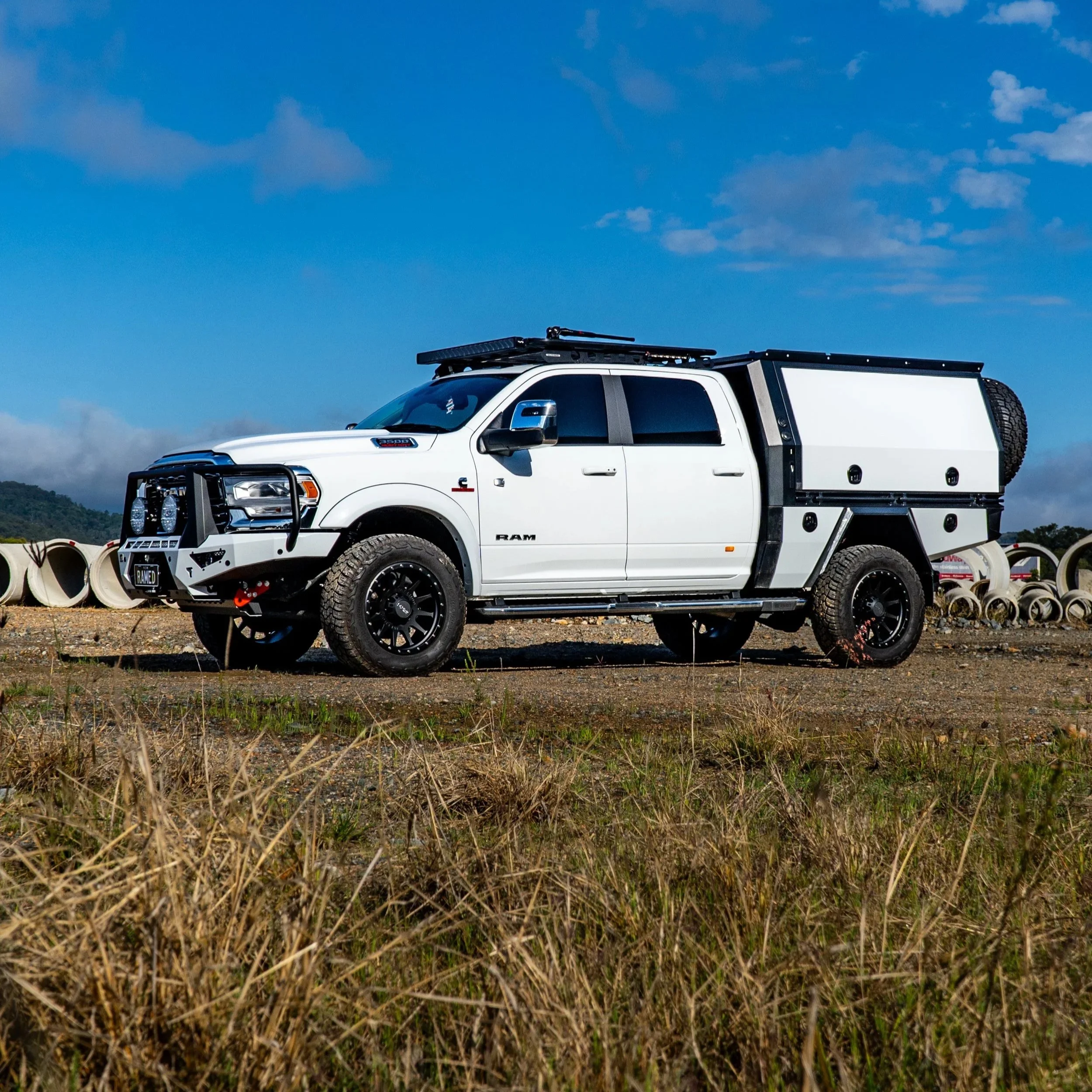 A white pickup truck parked on a gravel lot with a blue sky and some clouds above, surrounded by large concrete pipes.