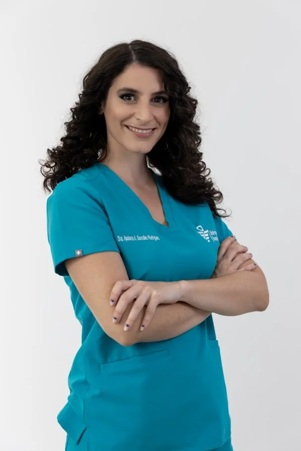 Woman in teal medical scrubs smiling with arms crossed against a white background.