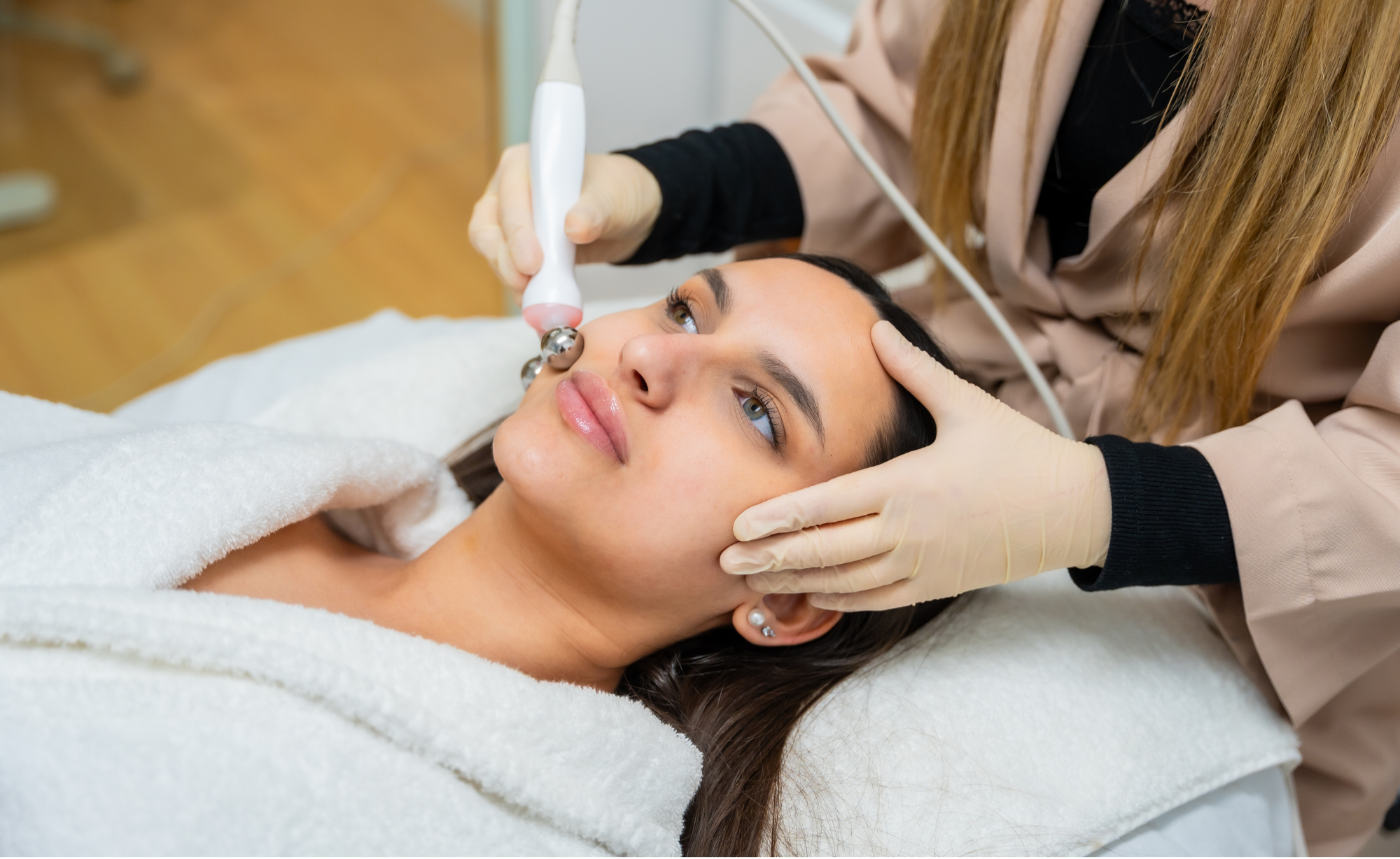 A woman receiving a facial treatment with a handheld device from a professional in a spa or clinic setting.