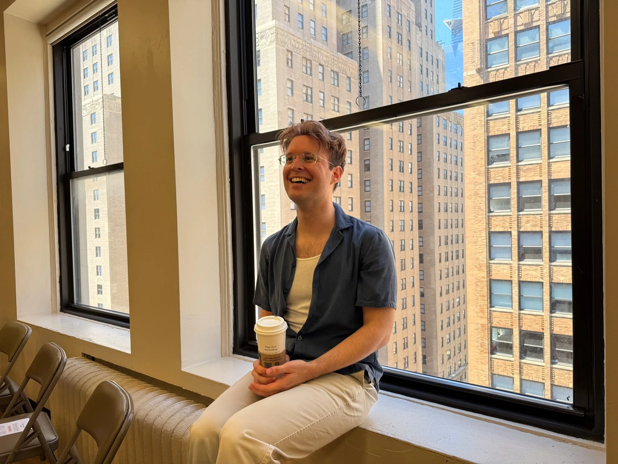 Man sits near a window and smiles with coffee