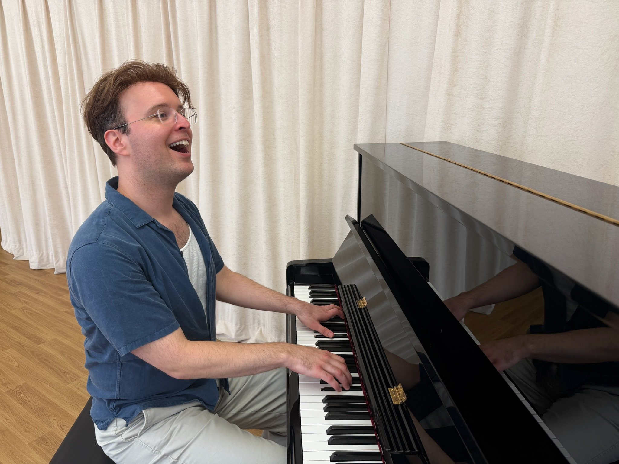 Man in blue shirt plays the piano while smiling.