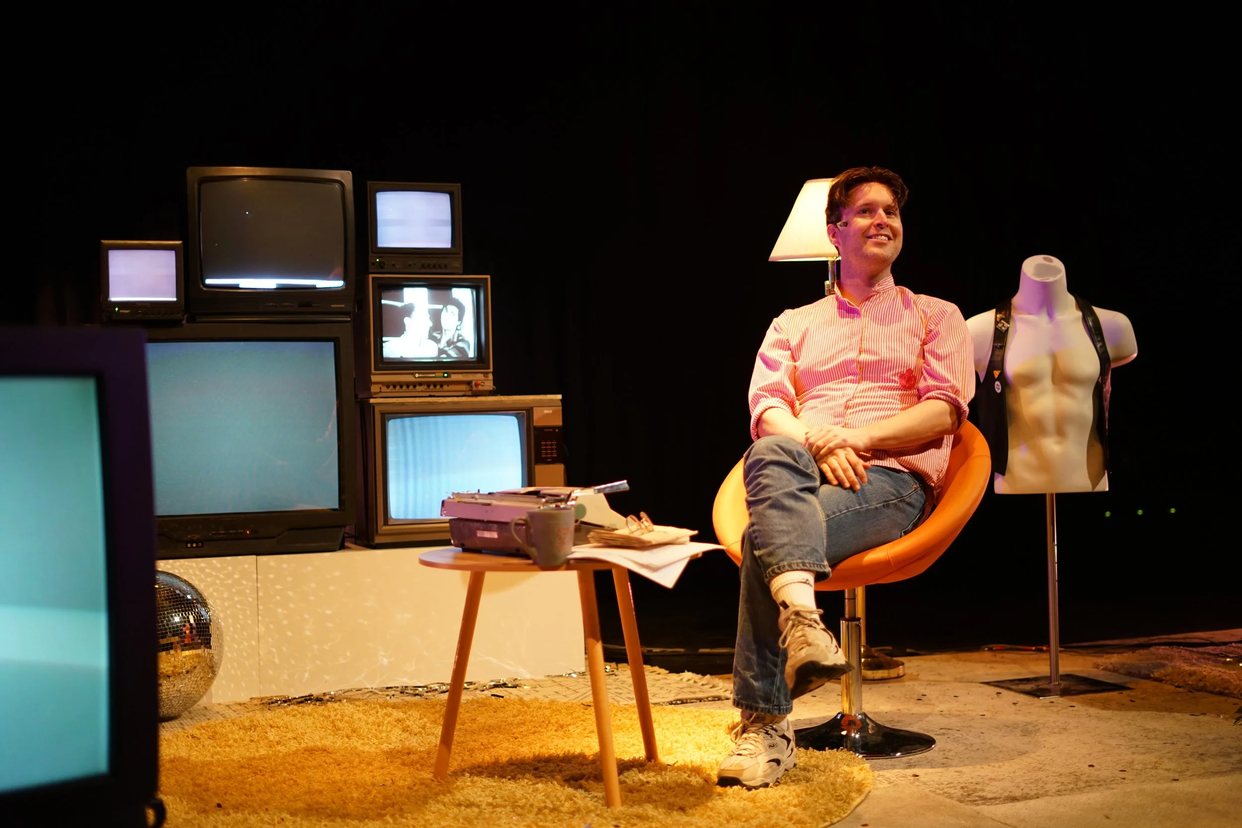 Man sits in chair on stage surrounded by televisions