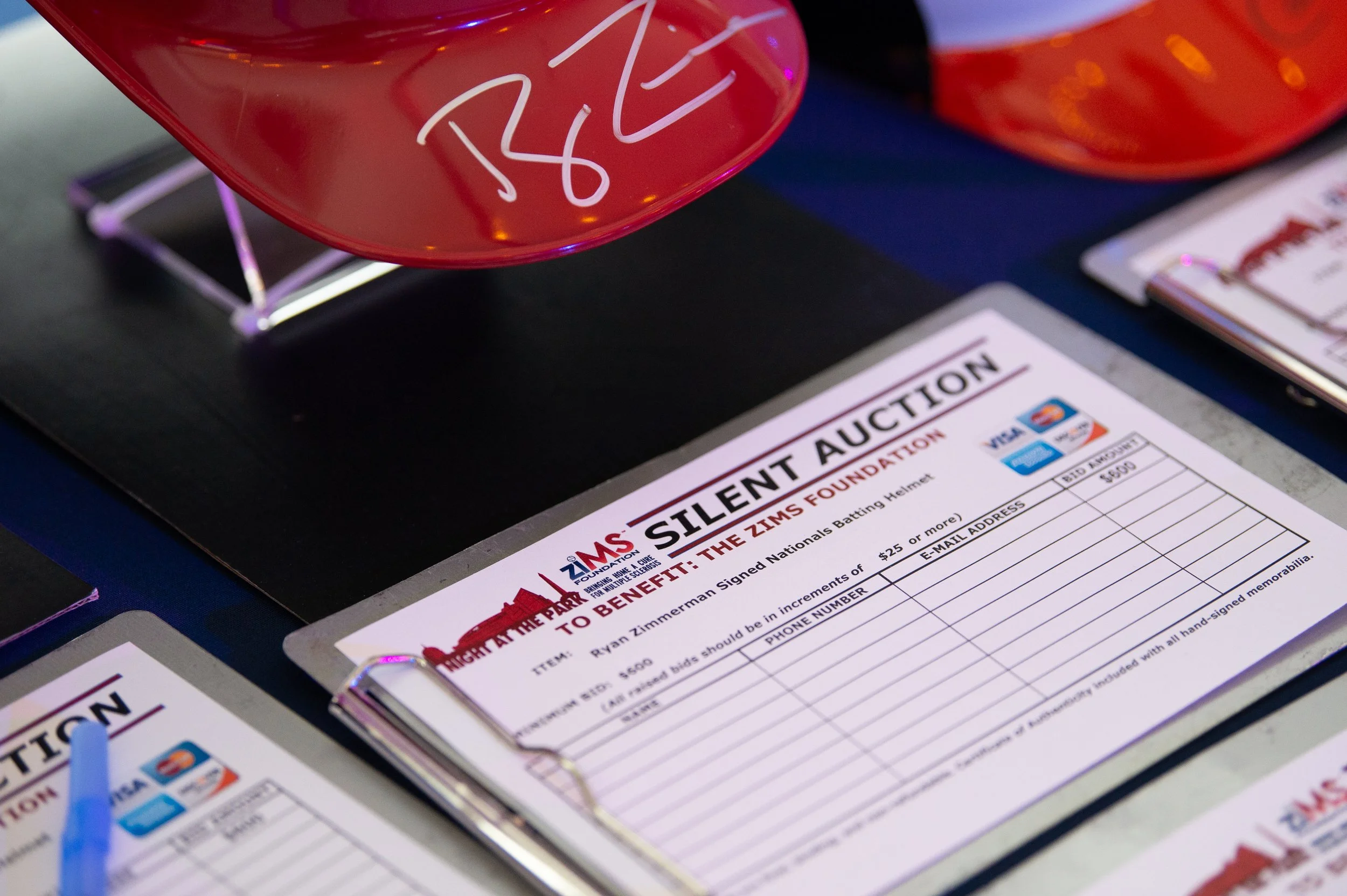 Close-up of an auction sheet and a red item with white signature on it, displayed on a table at an auction event.