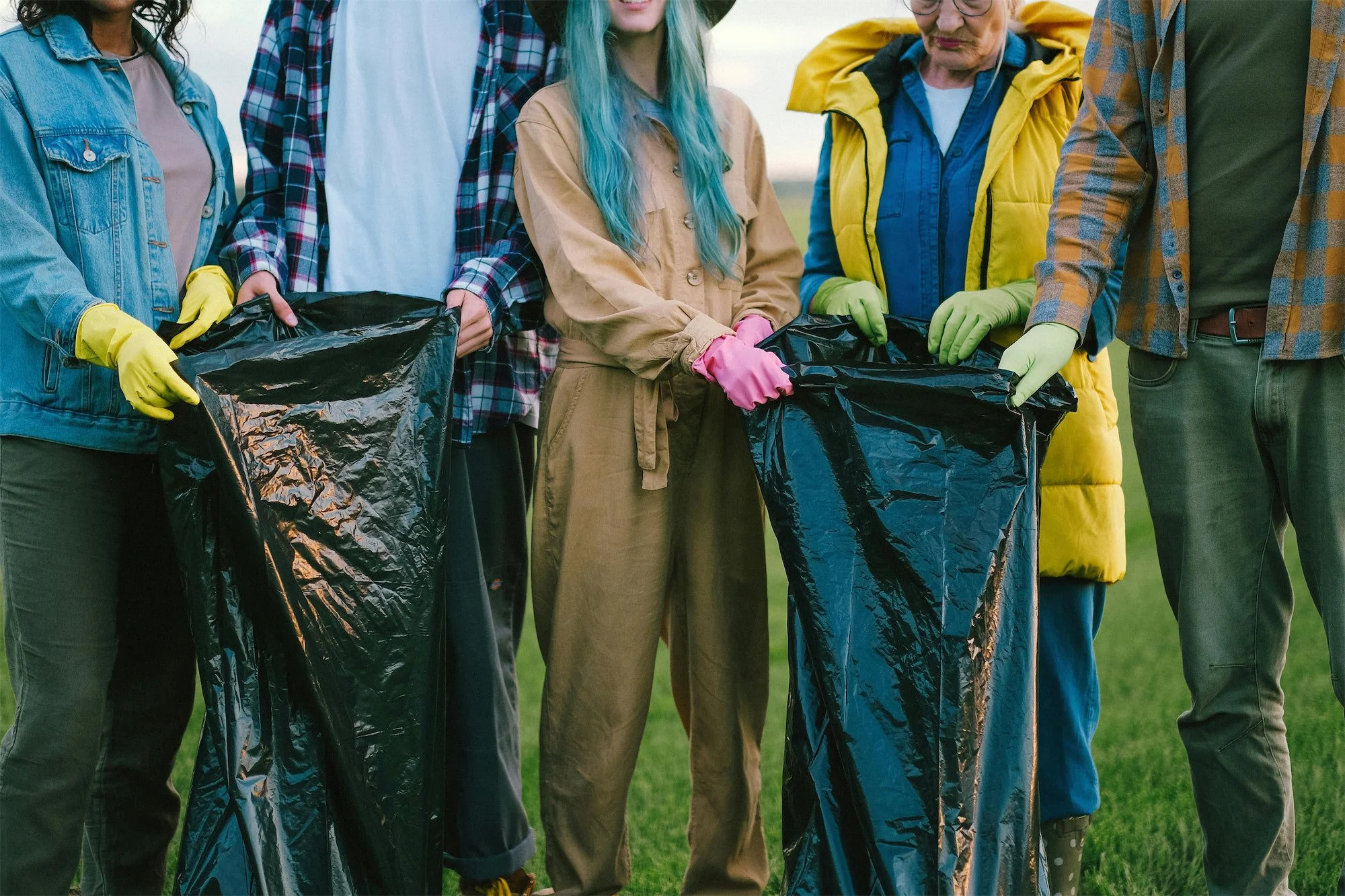 Group of people holding trash bags wearing gardening gloves outdoors.