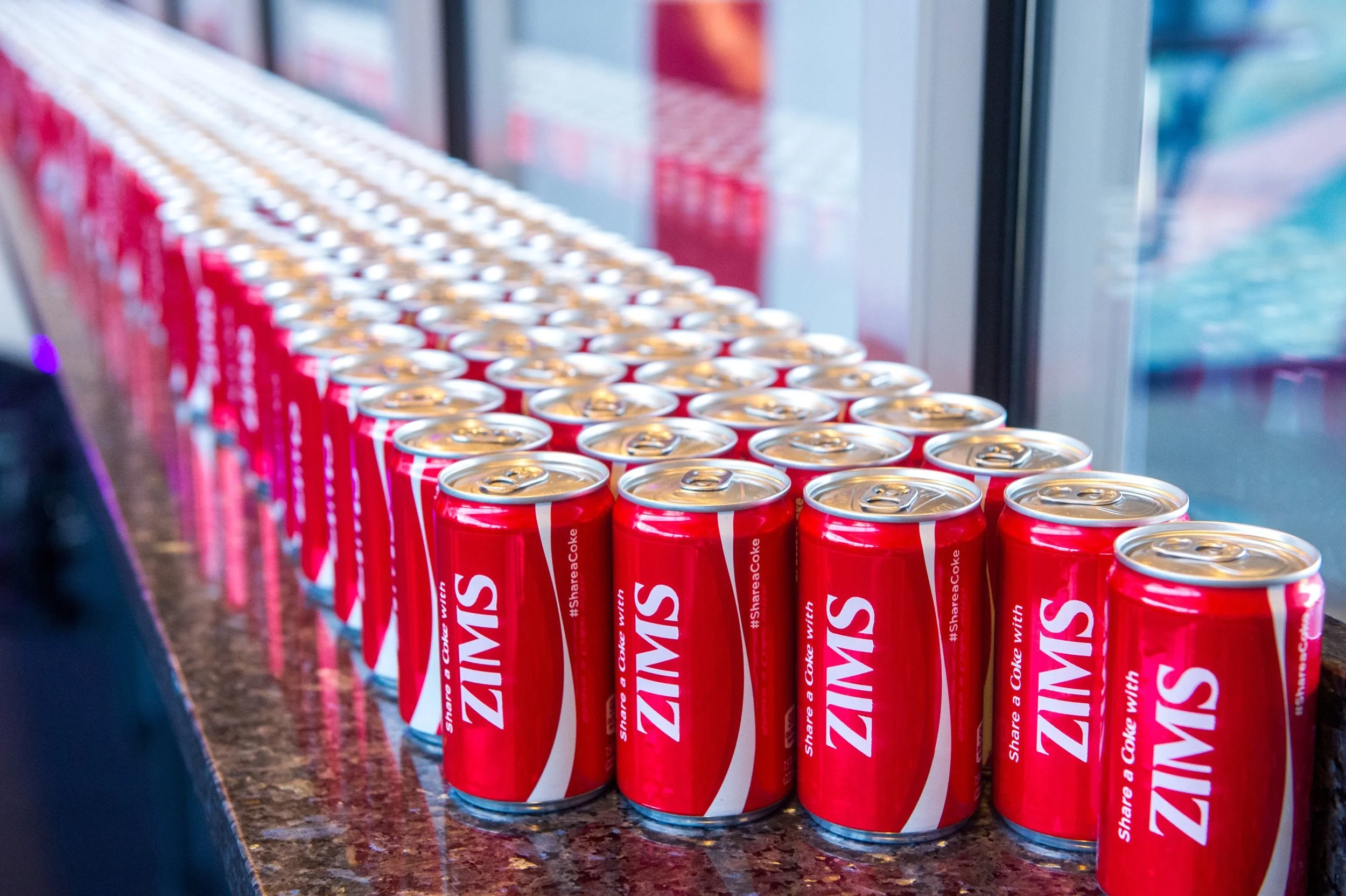 Rows of red cans of Coca-Cola featuring ziMS Foundation logo