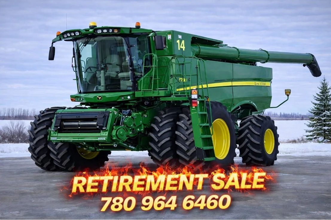 A large green John Deere combine harvester parked outdoors on a cold, snowy day with a cloudy sky, with bright yellow lettering advertising a retirement sale and a phone number.