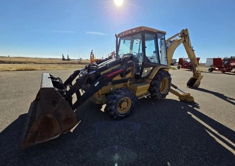 Yellow backhoe loader parked on asphalt under a bright sunny sky.