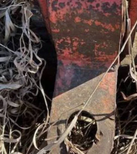 Close-up of a rusty, weathered metal pole with debris and dried plant material around it.