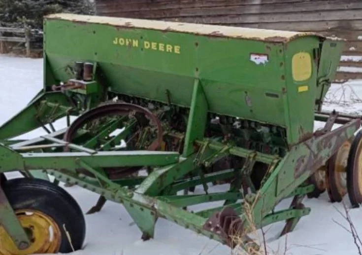 Old green John Deere farming equipment outdoors on snow, with rust and wear visible.