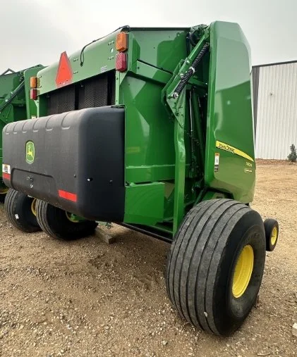 Green John Deere agricultural baler with large black and yellow tires, parked on a farm surface.