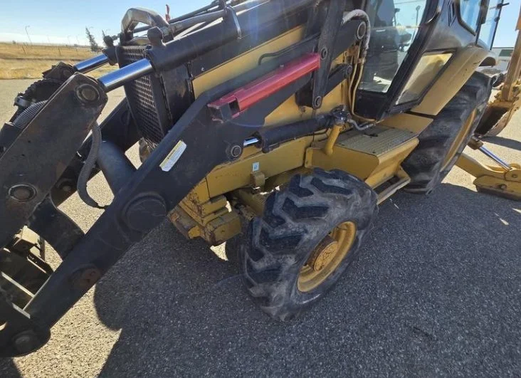 A yellow and black construction vehicle, likely a backhoe or loader, parked on a paved surface with a clear sky background.