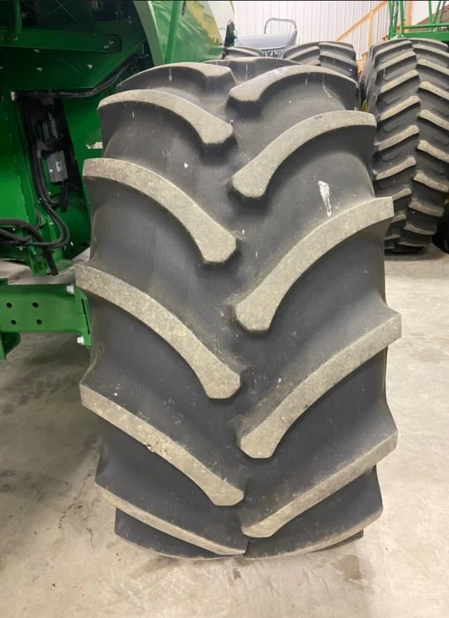 Close-up of a large agricultural tire with deep treads, mounted on a green tractor, with additional tires in the background.