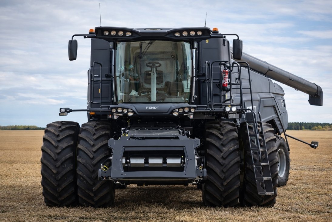 Large black harvesting machine in a field under a cloudy sky.