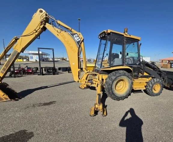 Yellow Caterpillar backhoe loader parked on asphalt surface under clear blue sky.