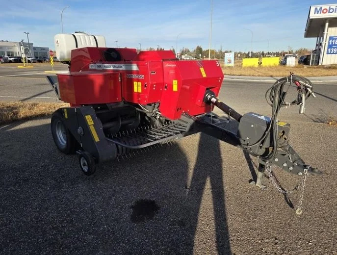 Red heavy-duty industrial street sweeper machine with a long hitch and black brushes underneath, parked on a gravel lot near a road.